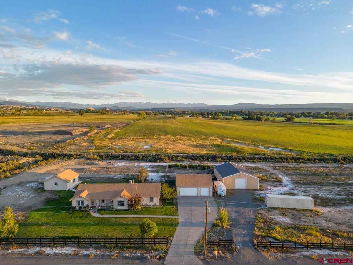Set on 2.95 acres across the street from the 18th Tee of the Bridges Golf & Country Club, this ranch-style 4BR/2BA offers a rare combination of space and convenience in one of Montrose’s most desirable settings with no restrictive covenants yet minutes from local amenities, grocery stores and the Rec Center. With three versatile outbuildings, it is a multi-use workshop compound uniquely offering great mountain views, plentiful interior and exterior storage and irrigated water for your landscaping and gardening needs. The 2,191sqft single-level home has a thoughtful floorplan, with a spacious primary suite and updated bathroom, formal living and dining rooms, an eat-in kitchen, three additional bedrooms, a full bathroom, a dedicated office/nursery, and a laundry room. Central heating and cooling keep you comfortable year-round with no HOA dues. Step outside to the south-facing backyard, where a covered, wired gazebo and 220V hookup set the stage for entertaining and a future hot tub. For the contractor, hobbyist, car enthusiast, or home-based business owner, the outbuildings are priceless. A 24'×32' insulated two-car garage, a 32'×36' three-car garage with tape-and-textured interior and 220V, and a 40'×60' heated shop with closed-cell insulation, plumbing, a 12'×12' door, 220V, and a 12'×20' climate-controlled room featuring an epoxy floor and dual heaters (36K + 18K BTU) combine for a great opportunity to curate the space and infrastructure to bring your vision to life.  Seller Financing options for qualified Buyers - inquire with broker and call today for your tour.