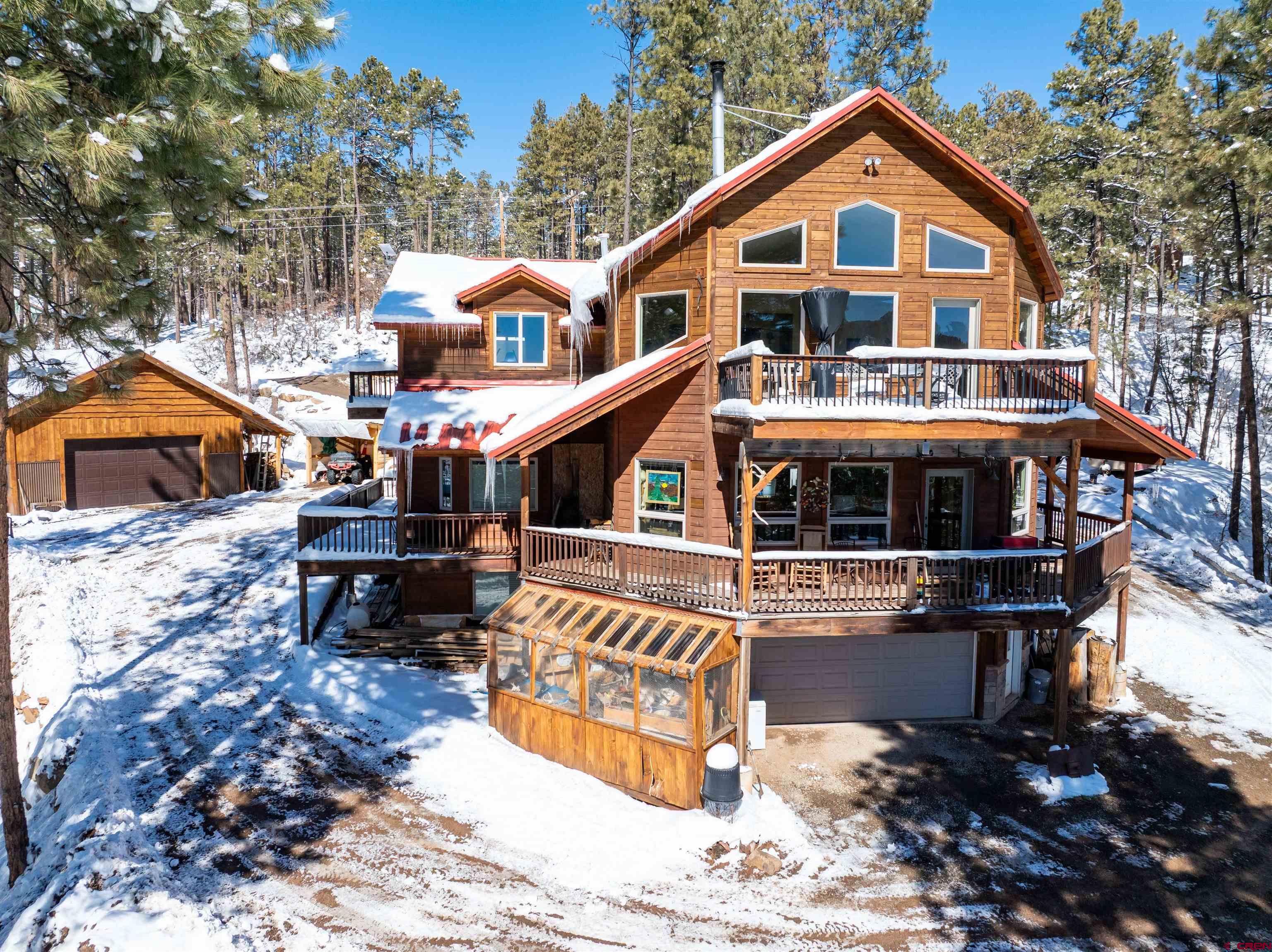 Tucked into the tall pines on a private two-acre parcel in the desirable Forest Lakes community, this three-bedroom + bonus room , 2.5-bath mountain retreat offers 2,654 square feet of thoughtfully designed living surrounded by mature trees and sweeping views of the Pine Valley. The setting delivers the quiet privacy buyers crave while remaining conveniently located between Durango and Bayfield on maintained roads. Inside, the home blends warmth, efficiency, and character. The main level offers an open floor plan where the living room, kitchen, and dining room surround a wall of windows facing the distant valley. The kitchen is anchored by rare, one-of-a-kind bullnose-finished granite countertops, extra deep sink and rich hardwood flooring, creating a space that feels both elevated and inviting. Natural light pours in, connecting the indoors to the surrounding landscape, where you can enjoy the wonderful wrap around deck year-round. The main-level primary suite offers true comfort with in-floor radiant heat and a spa-inspired heated-air bubble tub powered by its own dedicated water heater, as well as a floor-to-ceiling glass shower and custom cabinetry. Upstairs, the loft features a Juliet balcony, a guest bedroom, and a massive bonus room that provides flexibility for guests, hobbies, or work-from-home needs. The attached 2 car garage is convenient for everyday use, and the greenhouse is ideal for protecting seasonal vegetables. Outside, the property is equally impressive with multi-level parking and a purged lot that provides additional usable space. The huge shop houses the paid-off solar system that powers the home and detached garage, helping keep utilities low. The detached 4 car garage/shop also includes a full workshop and stove, while an additional storage building keeps equipment dry and ready, separate from your personal hobby zone or outdoor gear. Residents of Forest Lakes enjoy access to Lake Simpatico, a private stocked lake ideal for catch-and-release fishing and non-motorized recreation, as well as frisbee golf, a picnic area, a playground, and maintained greenbelt and trail areas woven throughout the neighborhood. In move-in-ready condition, this property offers the rare combination of privacy, infrastructure, efficiency, views, and established community amenities—mountain living without compromise. Additional upgrades include on-demand hot water, a brand-new dishwasher, and an updated septic system for peace of mind.