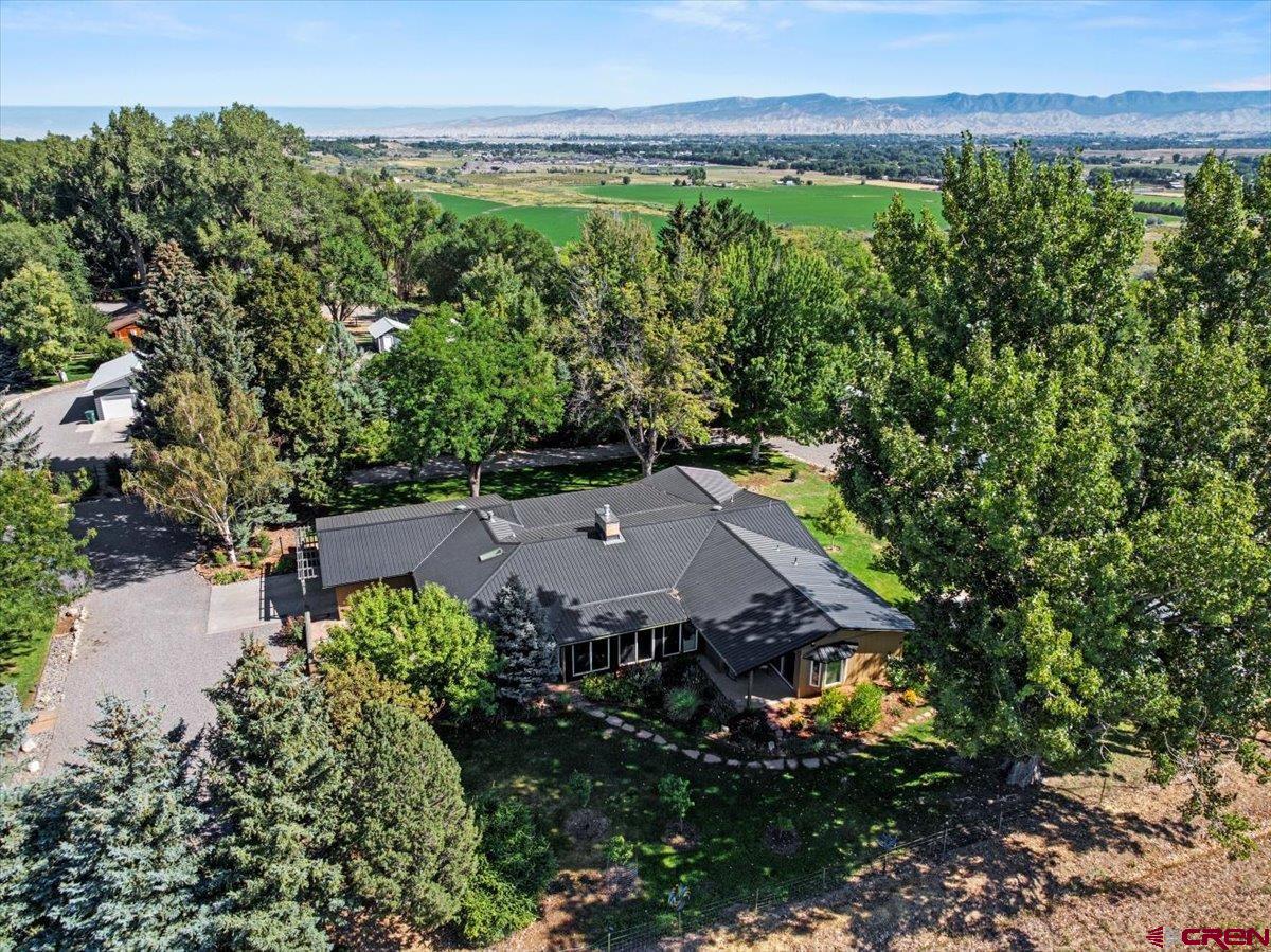 Charming Montrose Colorado Homestead on 2 Irrigated Acres – Single-Level Living at Its Best  Discover one of Montrose, Colorado’s most sought-after lifestyles with this rare single-level home on 2 irrigated acres perched on the Spring Creek Mesa escarpment. Just 10 minutes from downtown Montrose, this property combines modern comfort, impeccable condition, and a true Colorado homestead lifestyle.  Your private entry begins across a quaint bridge with a canal flowing beneath, leading to a lush, tree-shaded yard that feels private, pastoral, and serene. Designed for both relaxation and productivity, this property includes separately fenced garden and orchard areas, raised beds, a geodesic dome greenhouse, and a charming barn perfect for chickens or small livestock. With irrigation water rights, you’ll have everything you need to keep your gardens, orchard, and landscaping thriving year-round.  At the heart of this property is a beautifully designed single-level residence that blends functionality with architectural elegance. The light-filled sunroom welcomes you home and flows naturally into the open living spaces. A gourmet chef’s kitchen serves as the centerpiece, featuring radiant stone countertops, premium stainless appliances, a richly sized center island with prep sink, custom cabinetry, double ovens, and even dual dishwashers—ideal for entertaining.  Throughout the home, you’ll find solid hardwood flooring, custom woodwork, and carefully crafted details. The living and dining rooms are anchored by a dramatic floor-to-ceiling natural gas fireplace, creating a warm and inviting gathering space. A clever guest suite offers privacy and morning light, complete with a beautifully finished travertine bath. The luxurious primary suite features a spa-inspired bathroom with soaking tub, glass shower, and direct access to a private stone patio with mountain views. An additional bedroom and bath complete the thoughtful floor plan, offering comfort and versatility for family or guests.  Practicality meets luxury with a deep garage that includes ample storage and houses the ultra-efficient in-floor hot water heating system. Outdoors, enjoy Sneffels Mountain views from the lawn, an intelligently designed orchard and garden, full sprinkler system, and custom landscaping. Every corner of this property reflects care, creativity, and excellent condition.  This is more than a home—it’s a self-sustaining Montrose homestead where modern comfort meets Colorado country living. Whether you’re gardening, raising chickens, or simply relaxing under the shade trees, you’ll find peace, productivity, and beauty here.  Schedule your private showing today and experience the perfect blend of single-level living, irrigated acreage, and Montrose lifestyle.