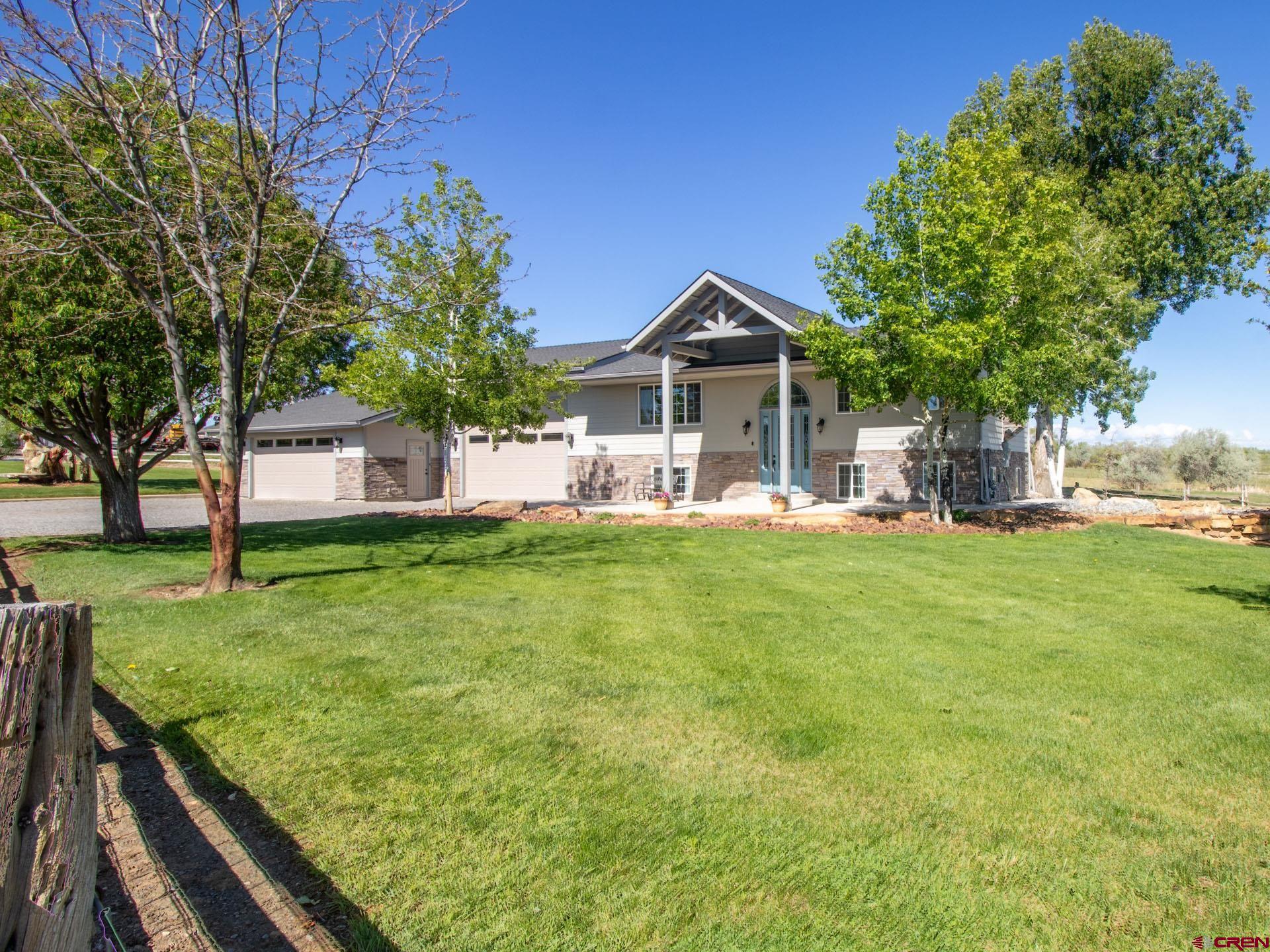 Situated on 3.622 acres in the highly desirable West Spring Creek area, this 2,360 square foot home offers a rare blend of country living, functionality, and beautifully maintained grounds. The 3-bedroom, 4-bathroom property features nearly 3 irrigated acres of productive hay field yielding approximately 200 bales annually, along with a separate .2-acre fenced horse or goat area. Over half an acre of manicured lawn and landscaping is supported by an automated sprinkler system and complemented by mature shade and fruit trees, creating a peaceful and picturesque setting with sweeping views of the Grand Mesa, Black Canyon Rim, and valley. The expansive open-concept living area showcases warm natural light, rich solid cherry cabinetry, and beautifully patterned bamboo flooring throughout. The gourmet kitchen is anchored by a massive center island topped with sleek black granite, offering abundant prep space, storage, and casual seating potential. High-end stainless steel KitchenAid appliances, including a double oven and warming drawer, under-cabinet accent lighting, custom tile backsplash, and soft-close pull-out drawers combine style and functionality for an elevated culinary experience. The seamless flow between the kitchen, dining, and living areas creates an inviting atmosphere ideal for entertaining, gatherings, or everyday comfort. Adjacent to the main living area is a versatile flex space offering endless possibilities for today’s lifestyle needs. Anchored by a cozy pellet stove, this inviting area could serve beautifully as a secondary living room, reading lounge, media space, or relaxed gathering area. A separate nook provides excellent potential for a home office or study area filled with natural light. The adjoining three-quarter bath features a modern dual vessel sink vanity, contemporary fixtures, and a beautifully tiled walk-in shower with glass enclosure, creating a stylish and functional extension of the living space. The garden-level primary suite offers a comfortable and private retreat with plush carpeting and dual ceiling fans. The en suite bath delivers a spa-like feel with a dual vanity featuring vessel sinks, a jetted soaking tub, and an impressive floor-to-ceiling tiled walk-in shower with sleek glass enclosure. A standout feature of the suite is the oversized walk-in closet, thoughtfully designed with custom built-ins and integrated drawers. Two additional bedrooms and an adjacent full bath complete the garden-level living area. Extensive covered front and rear patio spaces create exceptional outdoor living and entertaining areas thoughtfully designed to offer the perfect balance of sun and shade throughout the day. A separate dog yard area includes a landscaped block-wall enclosure with low-maintenance artificial turf, providing a clean and functional space for pets. An added 360-square-foot heated and cooled flex space in the garage, complete with an adjacent half bath, offers excellent versatility for use as an additional living area, gym, craft room, studio, or workspace. The 4+ car garage also features a 16' x 11' RV overhead door for added convenience and storage flexibility. Additional parking is close by with an 18’ x 80’ graveled RV pad. Combining luxury, flexibility, and productive acreage, this exceptional West Spring Creek property offers the very best of Colorado country living.