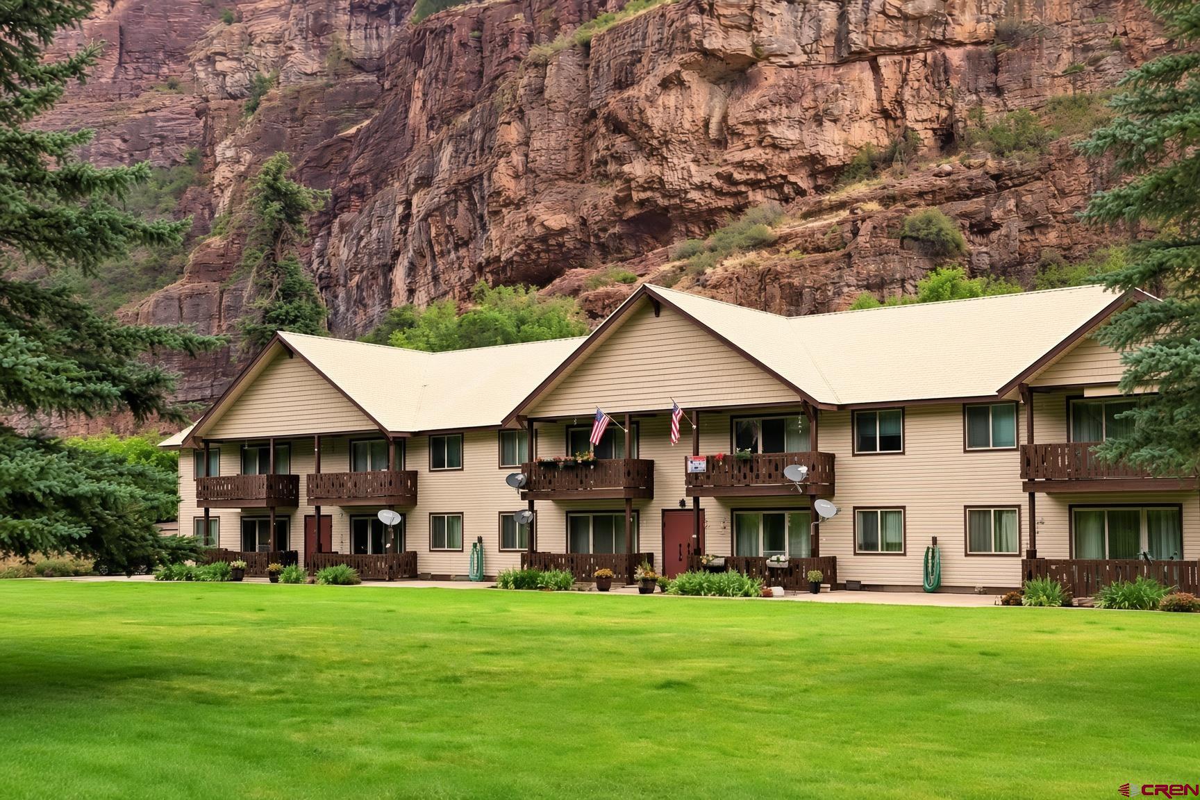 Ground Floor Condo in Krisken Chalet Condos – Ouray, Colorado. This beautifully maintained and completely furnished (with a few exceptions) 2-bedroom, 1-bath condominium offers an exceptional opportunity for affordable mountain living in Ouray. Located on the ground floor with no stairs to climb, this 990 sq. ft. unit provides easy, single-level access and walks directly out to a gorgeous, expansive front common lawn area framed by towering pines and dramatic canyon walls. Inside, the home feels warm and inviting with Brazilian cherry laminate flooring. The thoughtful layout features two comfortable bedrooms, a living room, and a cozy kitchen.   Outside, enjoy your own private patio in the back for relaxing or entertaining, plus the expansive shared lawn and BBQ/grilling area. The HOA professionally maintains all common areas, landscaping, and amenities across the beautifully landscaped 3+ acre property. Each unit includes a dedicated carport, additional outside parking, storage space, and plenty of guest parking. Perfectly situated at the north entrance to the City of Ouray, this “lock-and-leave” condo is just a 3-minute drive to the heart of town. It’s an ideal primary residence, vacation home, or income-producing rental property. Take full advantage of Ouray’s world-class hot springs pool, shops, restaurants, skiing, hiking, jeeping, and endless mountain adventures—all while enjoying low-maintenance living surrounded by stunning natural beauty. Welcome to comfortable, convenient Colorado mountain living at its most affordable!