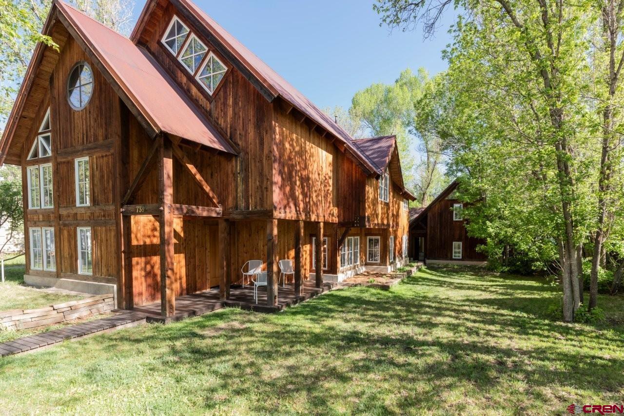 Opportunities to own one of Ridgway's truly iconic in-town homes are exceptionally rare, and this remarkable custom residence on coveted Clinton Street is among the finest. Long regarded as the premier residential block within Ridgway's Historic Town Center, Clinton Street is where timeless architecture, mature landscaping, and small-town charm come together just steps from the community's favorite destinations. Stroll a half block to Kate's Place for breakfast, meet friends at Colorado Boy Brew Pub, enjoy concerts and festivals in Hartwell Park, browse local galleries and boutiques, or walk to Mountain Market, Belle Vino, the library, schools, and restaurants. From this extraordinary location you're only minutes from Ridgway State Park, spectacular Ouray—the "Switzerland of America"—and an easy drive to the world-class skiing, golf, mountain biking, hiking, and internationally renowned music and film festivals of Telluride. Built by its owner in 2002 with uncompromising craftsmanship, the home possesses a warmth and character rarely found in newer construction. Set well back on an oversized, beautifully landscaped lot for exceptional privacy beneath mature shade trees, the property immediately captures attention with soaring rooflines, handcrafted cedar siding accented with reclaimed antique timbers, decorative ironwork, and architecture that feels both timeless and distinctly European. Inside, reclaimed old-growth redwood, gracefully curved walls, artisan millwork, custom doors, rich brick, tile, and wrought iron combine to create an atmosphere that is elegant, inviting, and unforgettable. Natural light pours through expansive windows, highlighting the remarkable craftsmanship throughout every room. The flowing floor plan was thoughtfully designed for both entertaining and everyday living, anchored by an extraordinary great room featuring a magnificent vintage 1890 wood-burning stove that fills the home with warmth and old-world character. The gourmet kitchen is worthy of a luxury magazine, showcasing a Viking professional range with custom iron surround, Viking double wall ovens, a 48-inch Sub-Zero refrigerator, richly crafted custom cabinetry, striking stained concrete countertops, beautiful artisan lighting, generous pantry space, and a charming built-in breakfast nook. A sculptural curved staircase leads to the private upper levels where the luxurious primary suite offers a spa-inspired bath with a European walk-in shower, oversized jetted soaking tub for two, and an impressive walk-in wardrobe with soaring ceilings and custom built-ins. A second bedroom with bath provides privacy for family or guests, while the upper loft overlooking the great room is ideal as a home office, media room, or third bedroom. Completing this exceptional property is a highly desirable detached carriage house featuring oversized garage and workshop space below and a beautifully finished one-bedroom, one-bath accessory dwelling above—perfect for guests, multigenerational living, long-term rental income, or short-term rental opportunities with appropriate approvals. Combining extraordinary craftsmanship, timeless architecture, income potential, and one of the most desirable walkable locations in Ridgway, this is a legacy property that seldom becomes available. For those who have admired this home for years while dreaming, "Someday that home will be mine," someday has finally arrived.