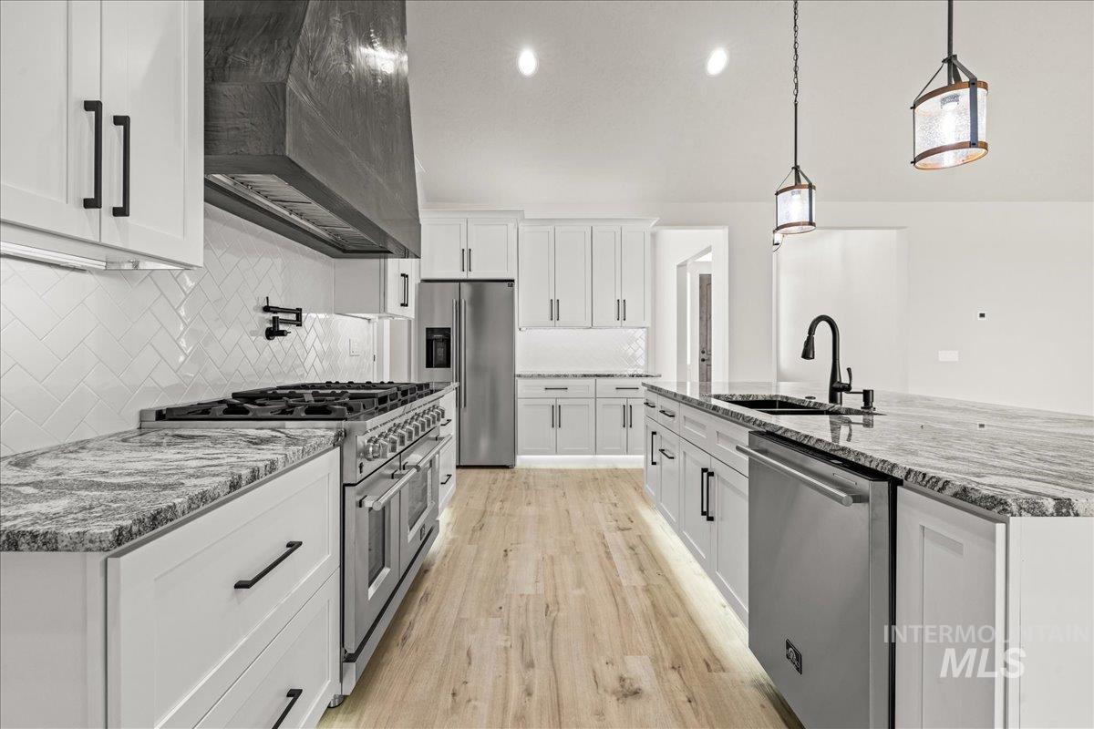 Kitchen featuring stainless steel appliances, decorative backsplash, custom range hood, light stone counters, and light wood-style floors