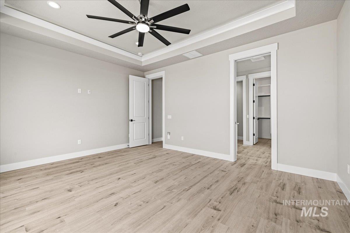 Unfurnished bedroom with a tray ceiling, light wood-style flooring, and ceiling fan