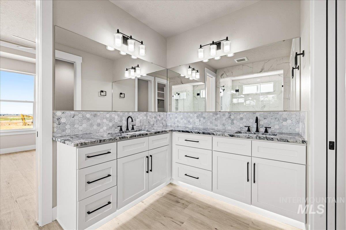 Bathroom featuring double vanity, backsplash, a marble finish shower, and light wood-style flooring