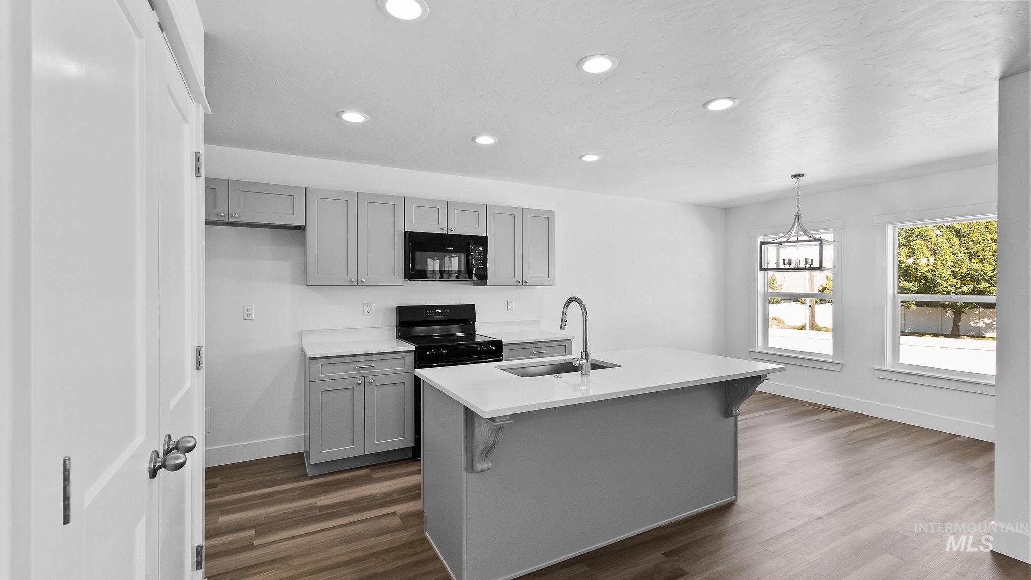 Kitchen with gray cabinetry, recessed lighting, dark wood-style flooring, black appliances, and an island with sink
