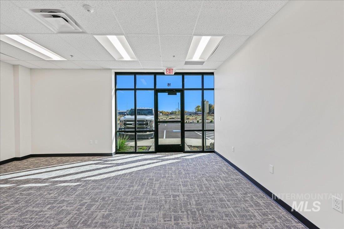 Carpeted empty room featuring a wall of windows and a drop ceiling