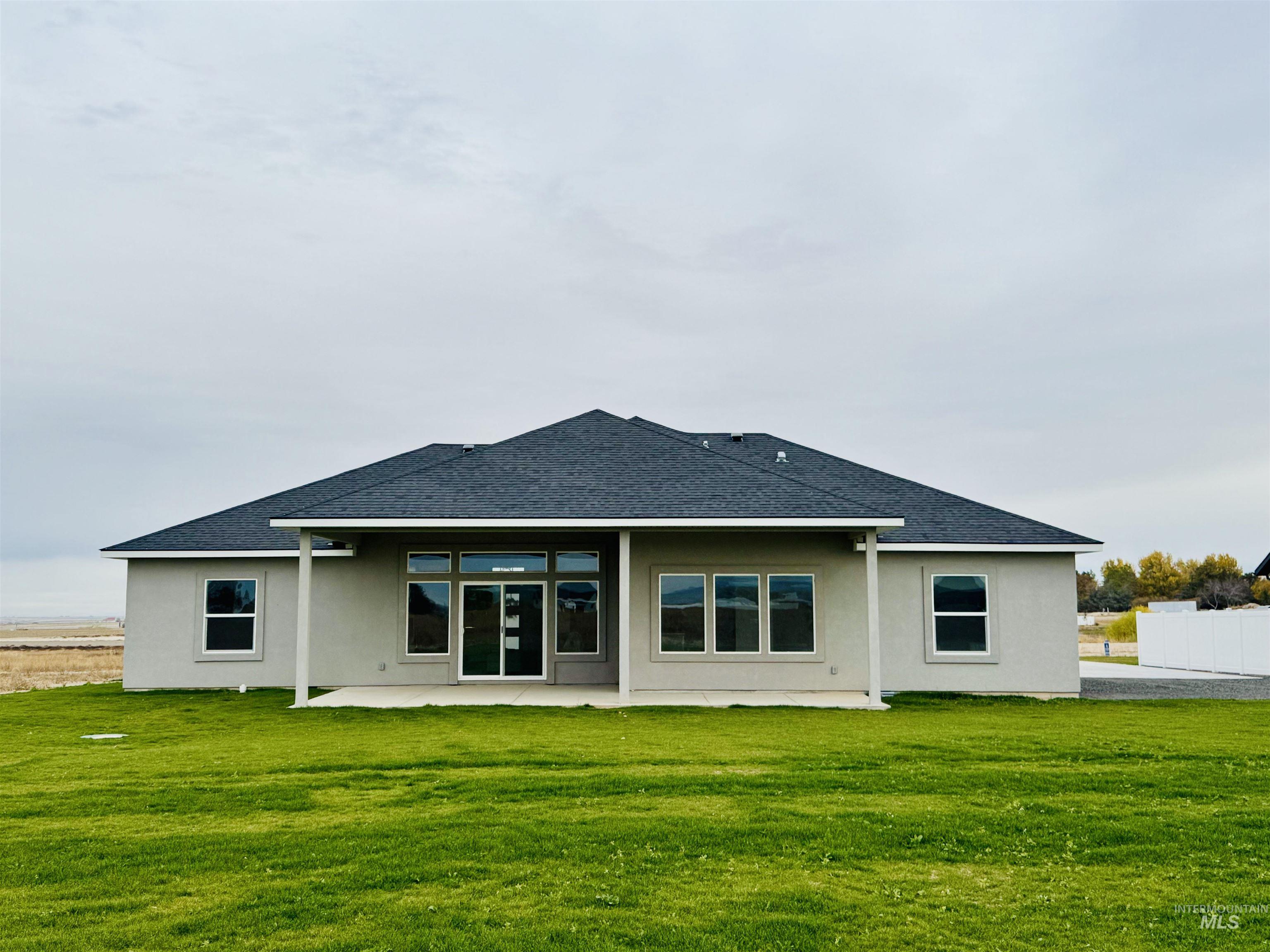 Rear view of house featuring roof with shingles, a lawn, a patio area, and stucco siding