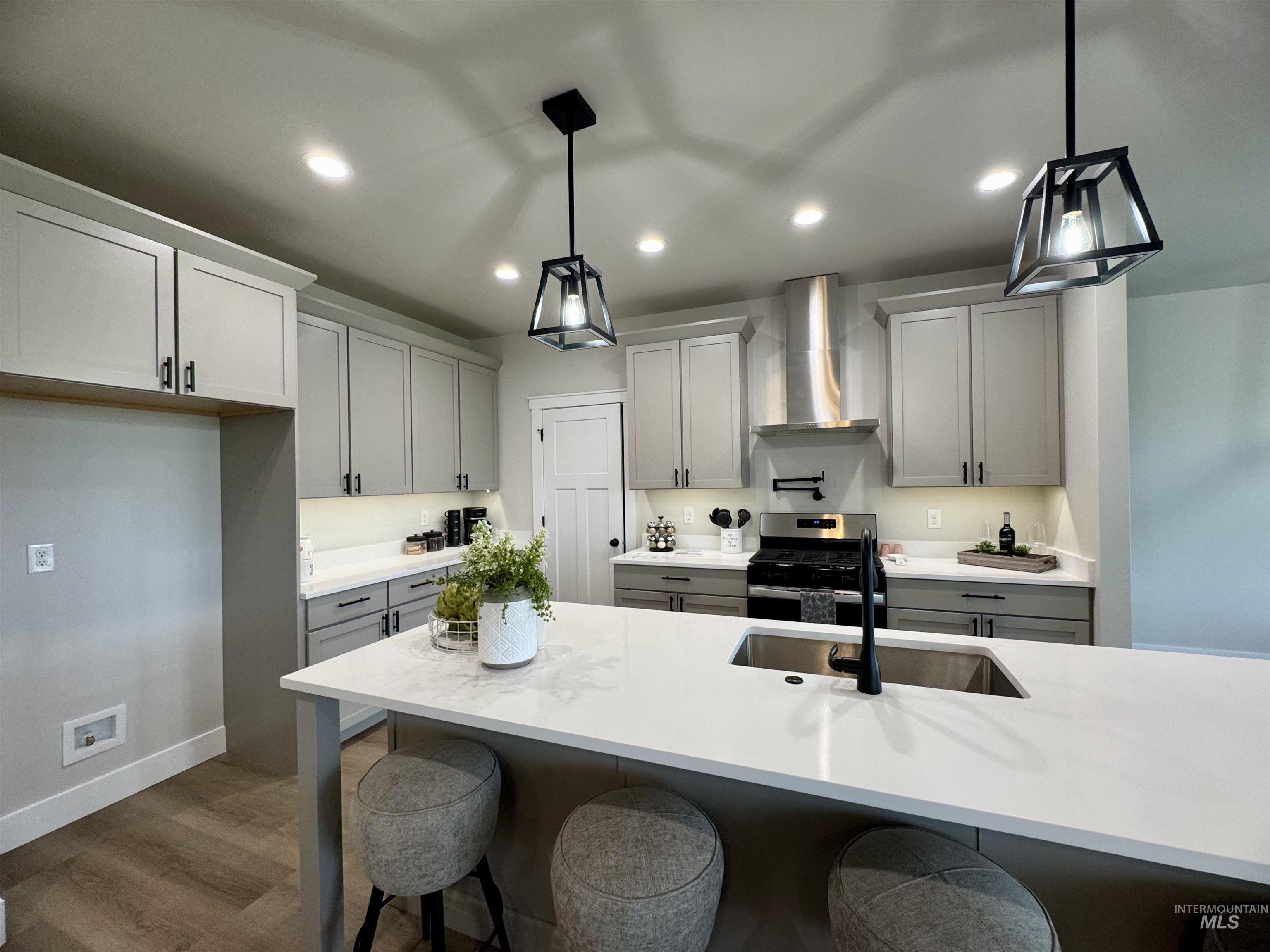 Kitchen featuring a breakfast bar, stainless steel gas stove, dark wood finished floors, wall chimney exhaust hood, and recessed lighting