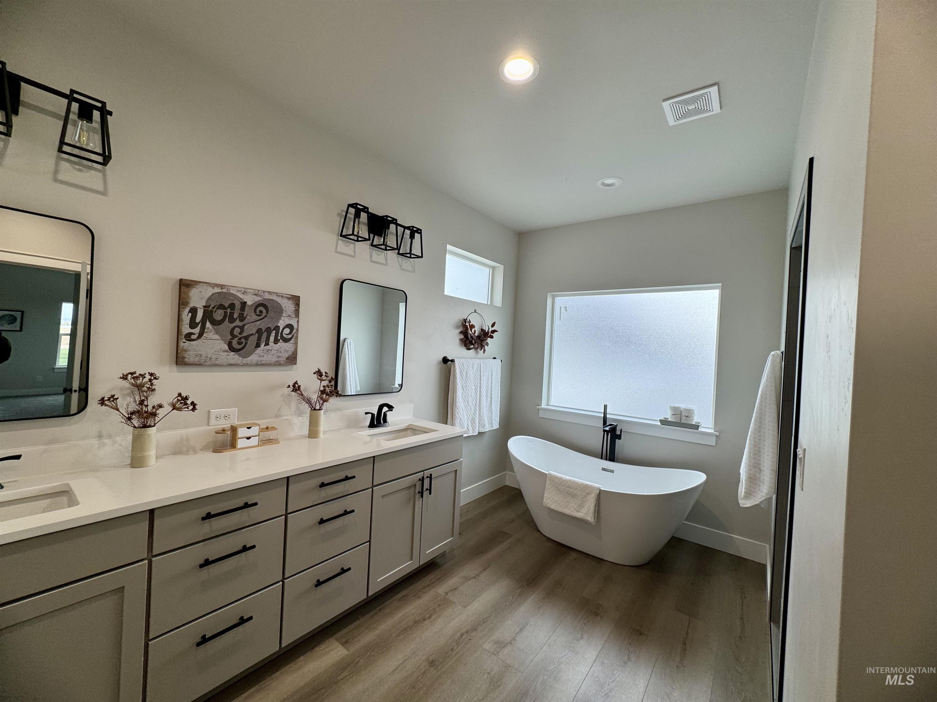 Bathroom with a freestanding tub, double vanity, light wood-type flooring, and recessed lighting