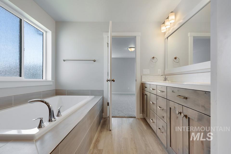 Bathroom featuring vanity, a garden tub, and wood finished floors