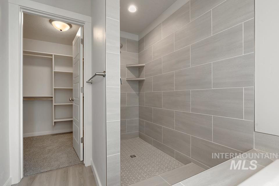 Full bathroom featuring tiled shower, a spacious closet, and wood finished floors