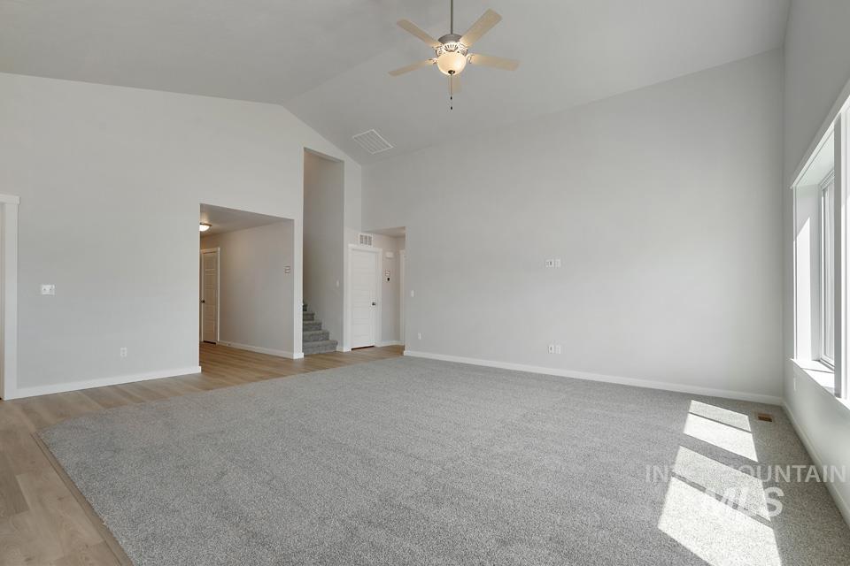 Unfurnished room featuring a ceiling fan, high vaulted ceiling, stairway, and light wood finished floors