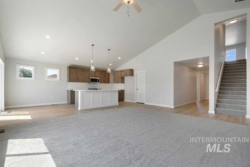 Unfurnished living room featuring stairway, light wood finished floors, a ceiling fan, and high vaulted ceiling