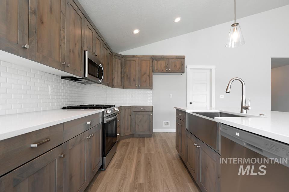 Kitchen with vaulted ceiling, appliances with stainless steel finishes, light countertops, light wood finished floors, and backsplash