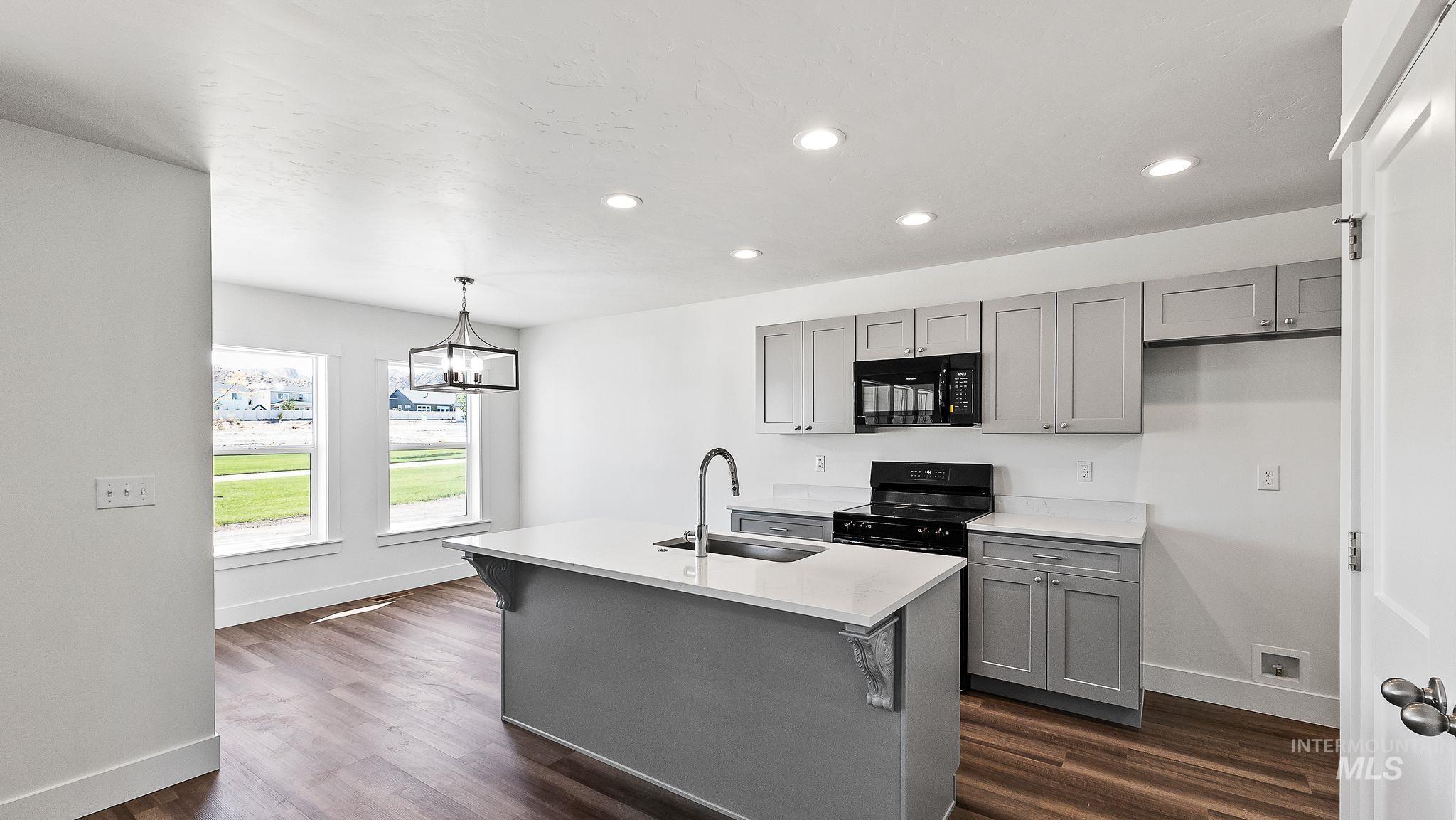Kitchen with gray cabinets, black appliances, recessed lighting, pendant lighting, and an island with sink
