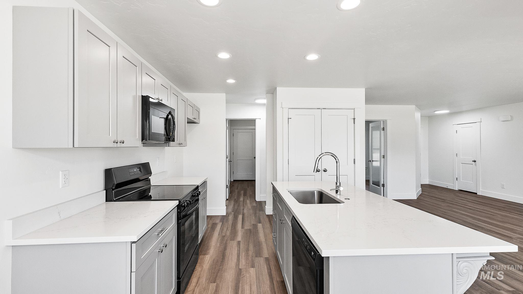 Kitchen with black appliances, recessed lighting, dark wood-style flooring, an island with sink, and light stone countertops