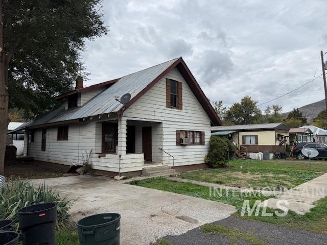 Bungalow with a chimney, a metal roof, a front lawn, and cooling unit