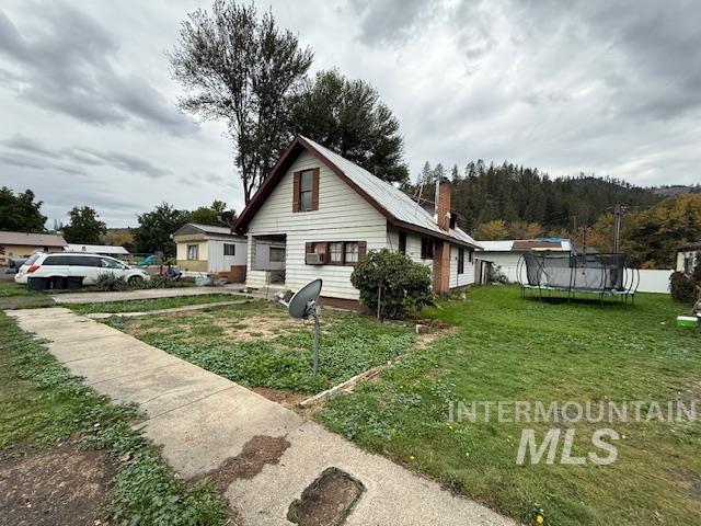 View of property exterior featuring a trampoline, a lawn, and a chimney