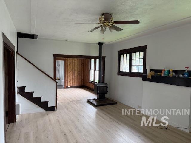 Unfurnished living room with a wood stove, light wood-style floors, stairway, and ceiling fan