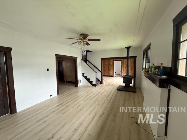 Unfurnished living room with a wood stove, light wood-style floors, stairs, and ceiling fan