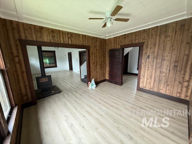 Unfurnished living room featuring wood walls, a wood stove, stairs, wood finished floors, and ceiling fan