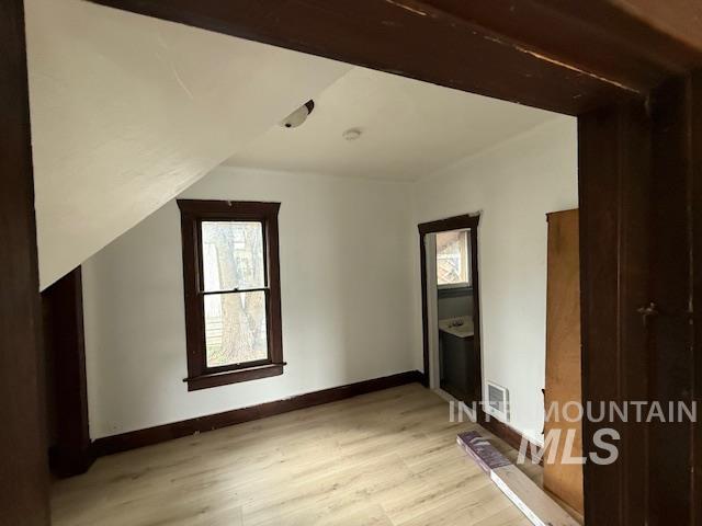Additional living space featuring healthy amount of natural light, light wood-style floors, and vaulted ceiling