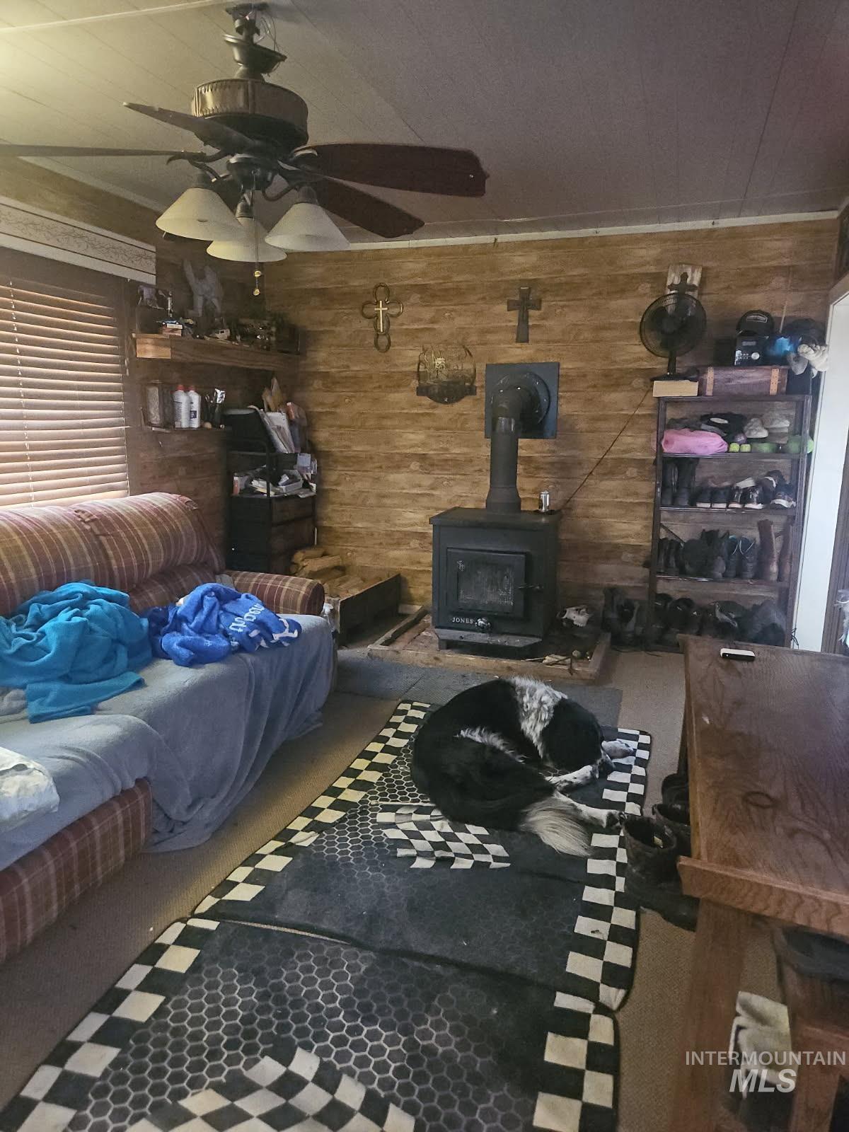 Living area featuring a wood stove, wooden walls, carpet floors, and a ceiling fan