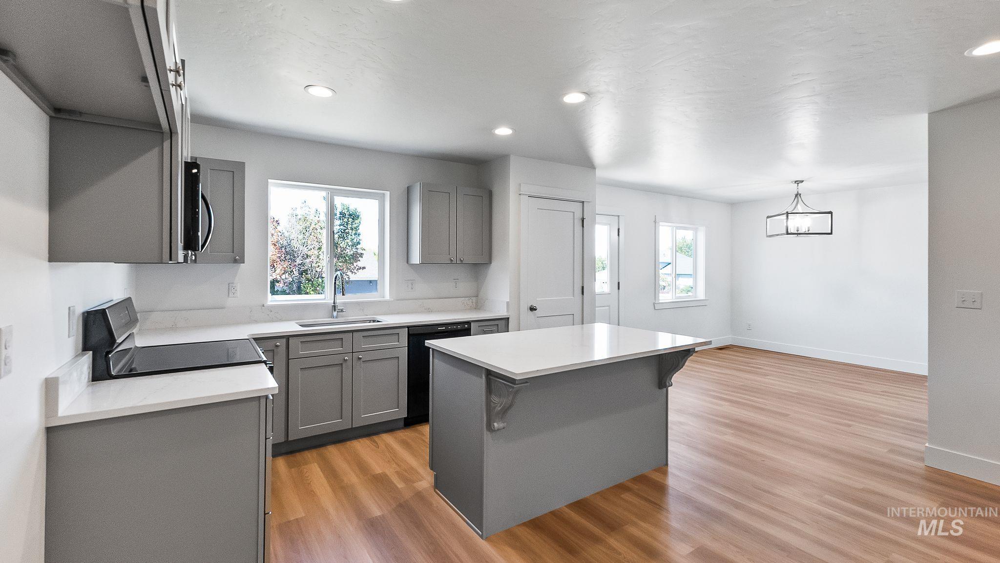 Kitchen featuring gray cabinetry, a kitchen island, electric stove, light wood finished floors, and a kitchen bar
