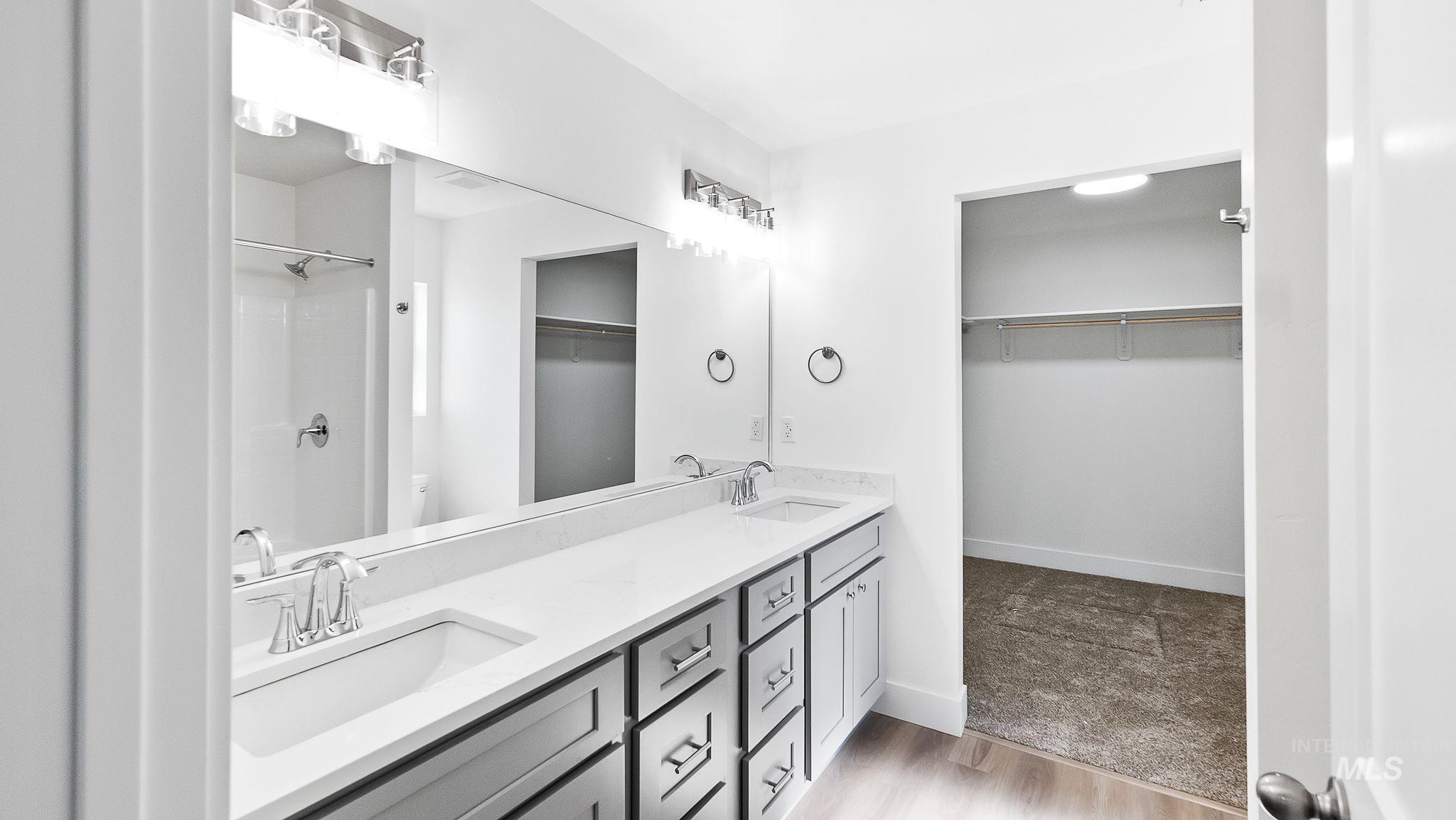 Full bathroom with a spacious closet, double vanity, light wood-type flooring, and a shower