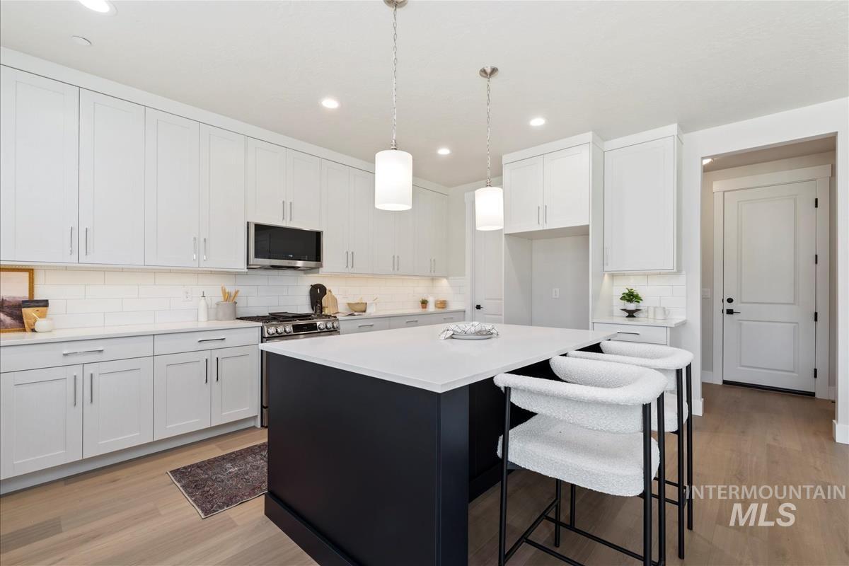 Kitchen with stainless steel appliances, a kitchen island, light countertops, decorative backsplash, and white cabinets
