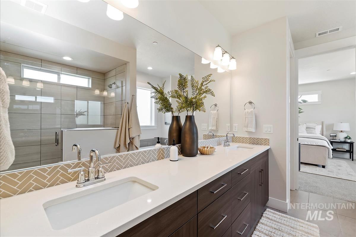 Ensuite bathroom with double vanity, a shower stall, and tile patterned floors