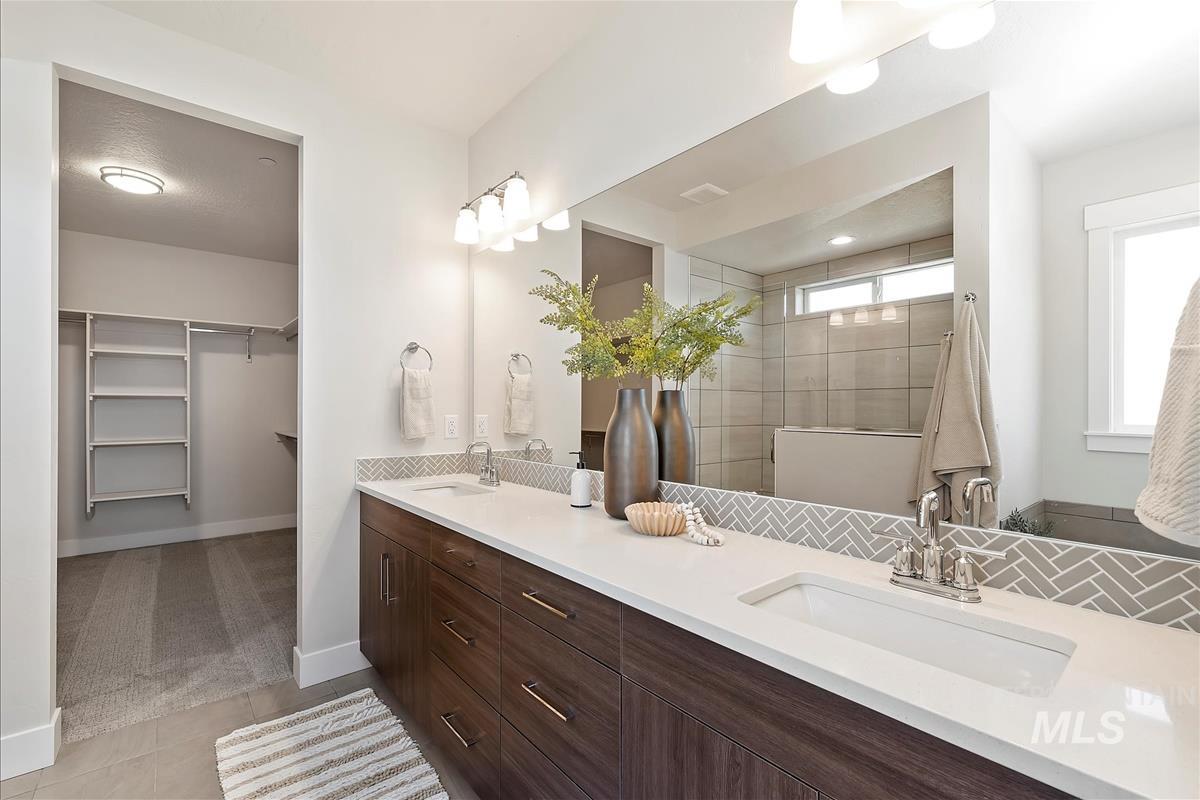 Bathroom featuring double vanity, a tile shower, a spacious closet, and tile patterned floors