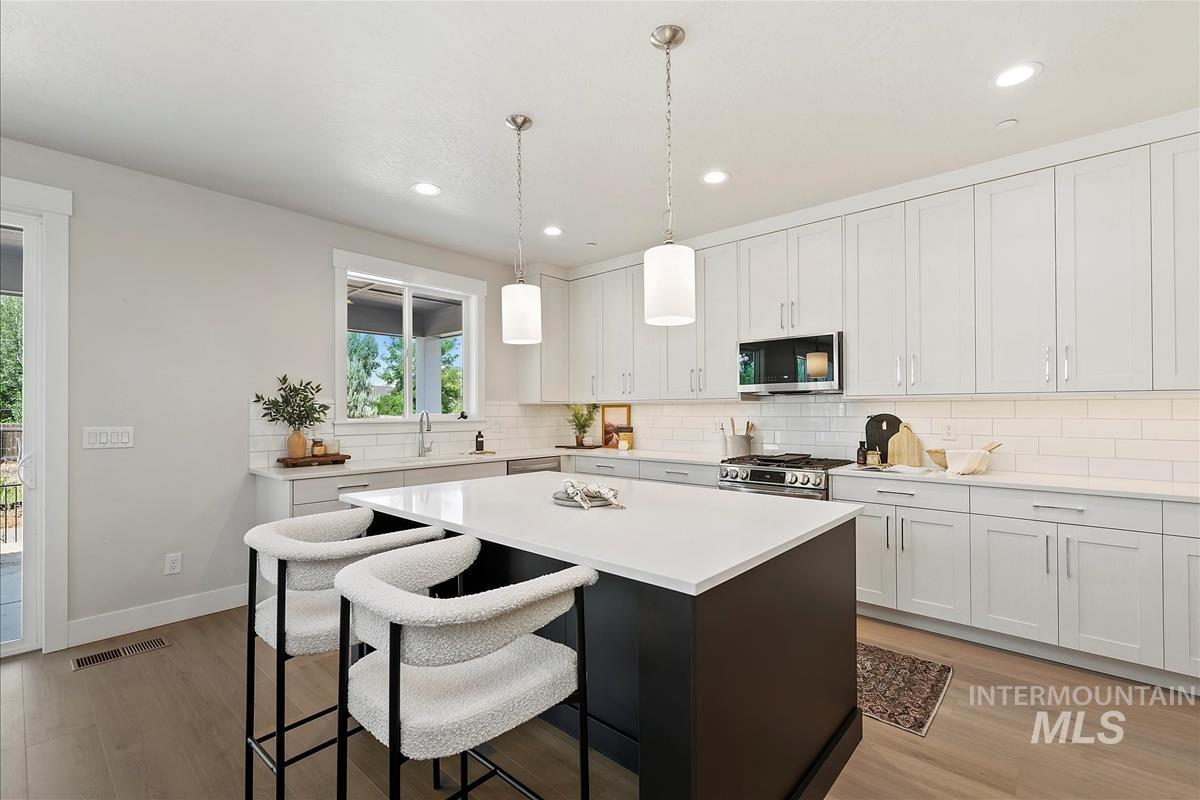 Kitchen featuring a breakfast bar, backsplash, light wood finished floors, a kitchen island, and light countertops