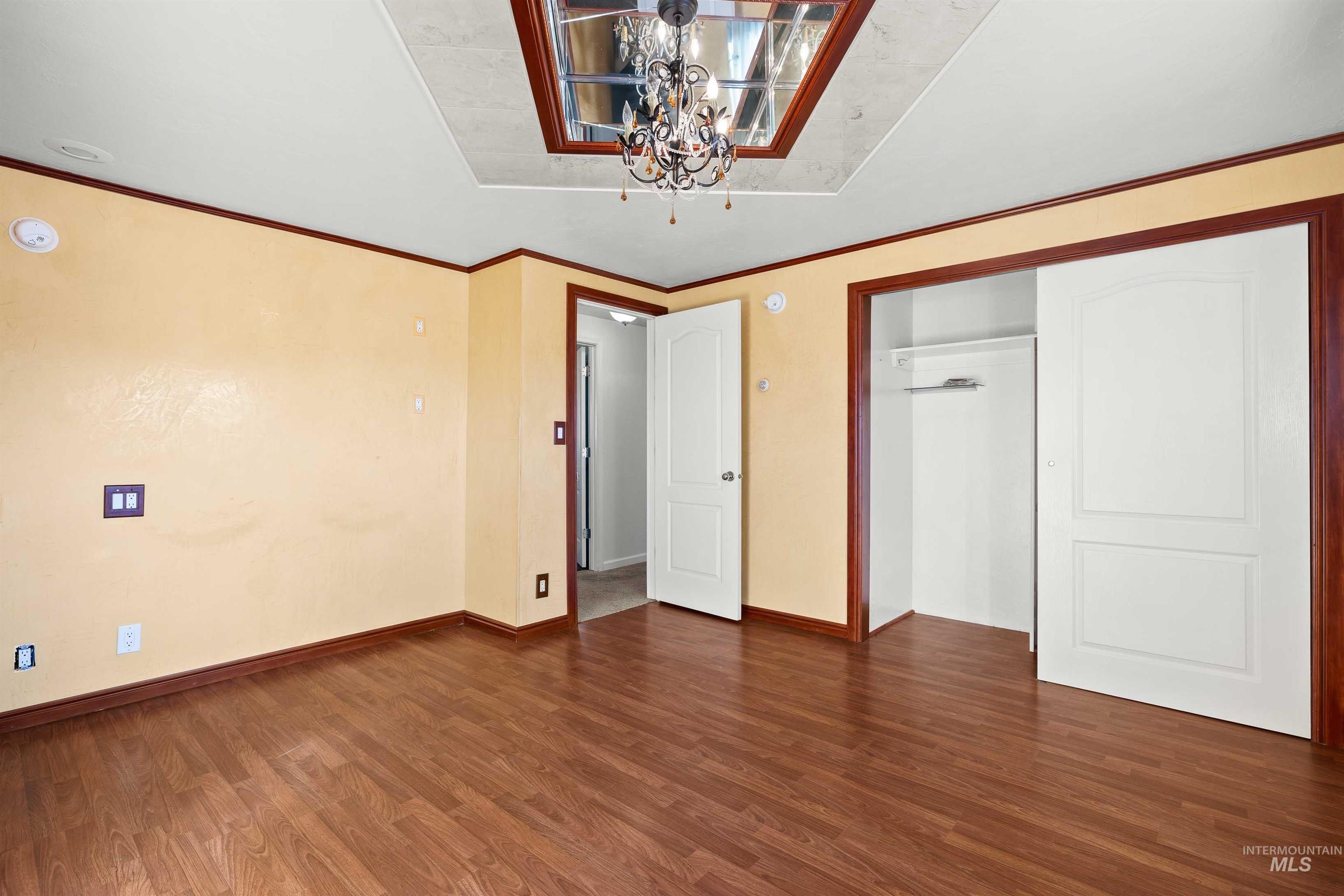 Unfurnished bedroom with ornamental molding, dark wood finished floors, a chandelier, and a closet