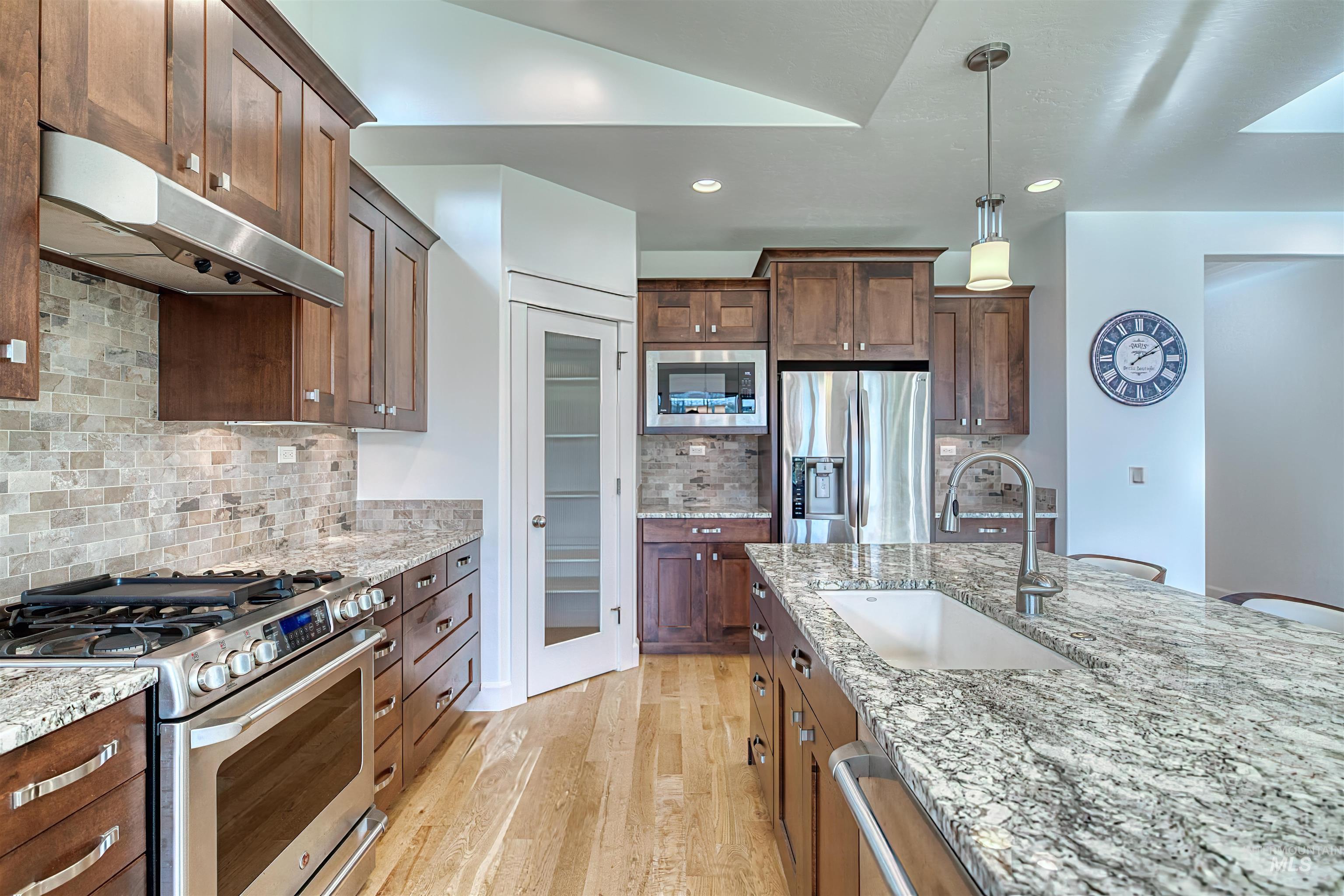 Kitchen featuring stainless steel appliances, under cabinet range hood, hanging light fixtures, light stone counters, and recessed lighting