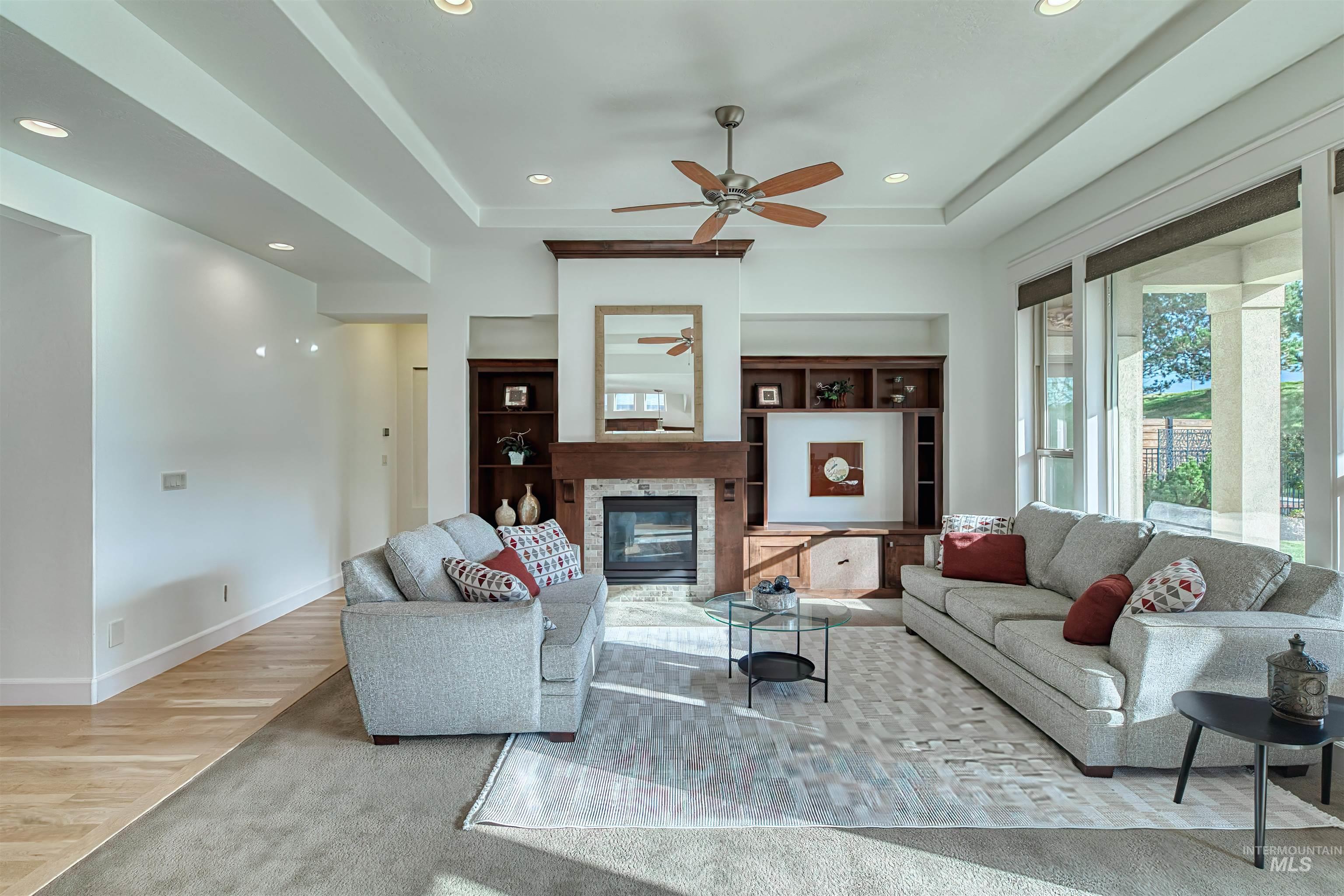 Living area with light wood-style flooring, recessed lighting, a glass covered fireplace, a tray ceiling, and ceiling fan