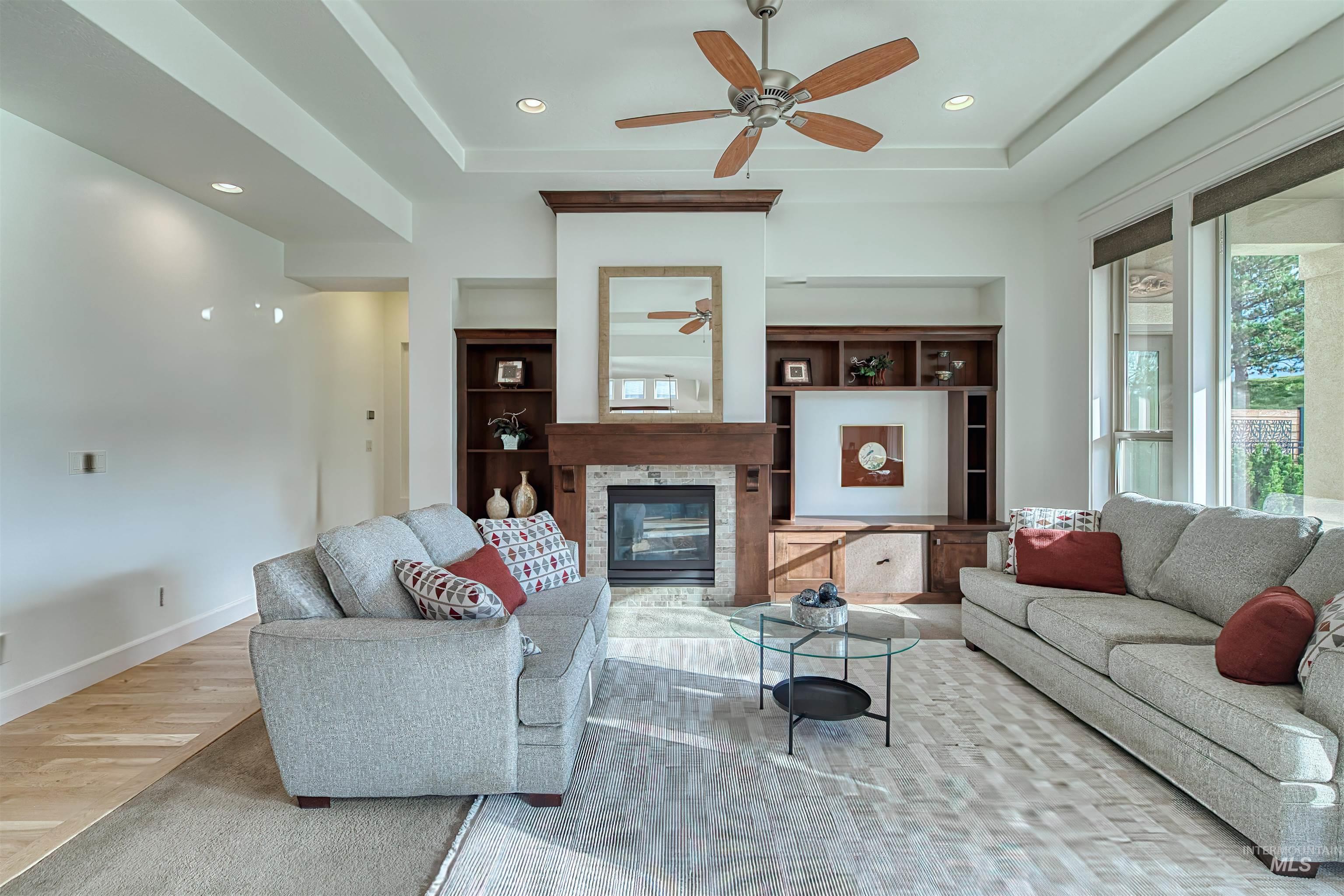 Living room with a glass covered fireplace, a tray ceiling, light wood finished floors, recessed lighting, and a ceiling fan