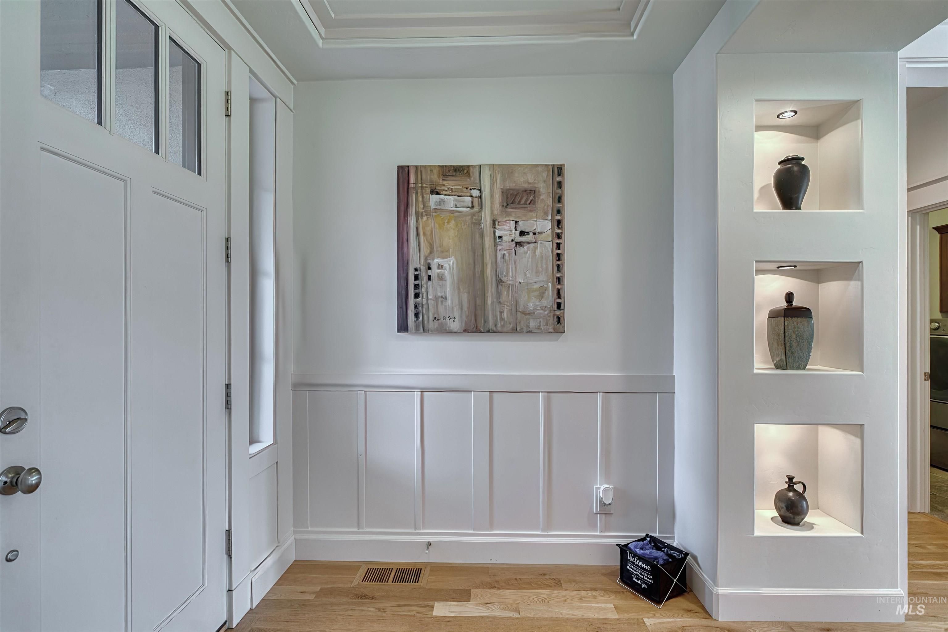 Corridor with light wood finished floors, a wainscoted wall, built in shelves, and a decorative wall