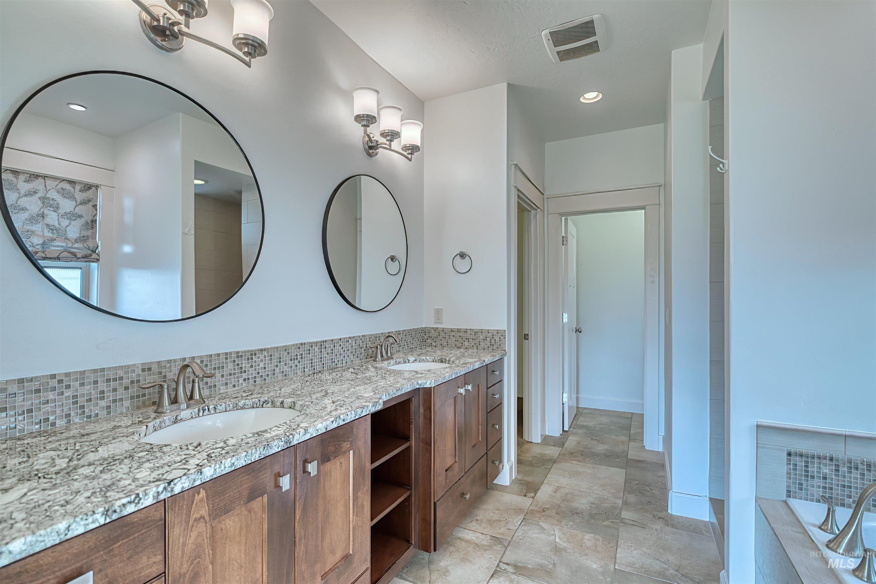 Bathroom featuring double vanity, tasteful backsplash, tiled bath, and recessed lighting