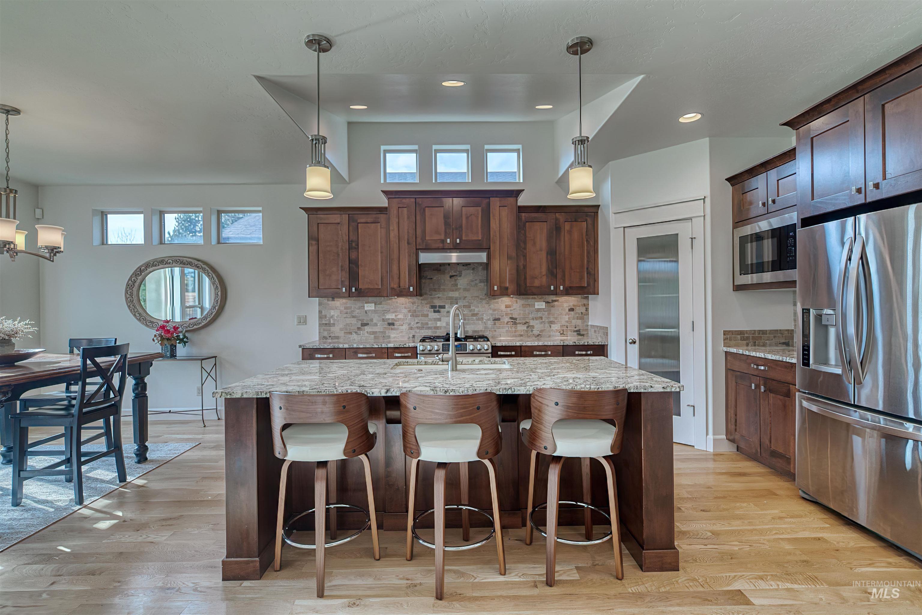 Kitchen featuring hanging light fixtures, stainless steel appliances, a breakfast bar area, light stone countertops, and tasteful backsplash