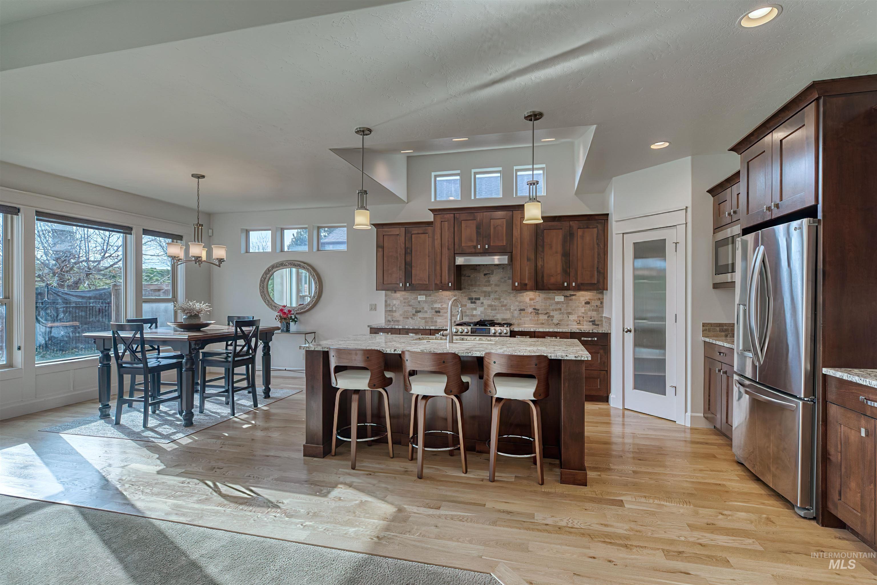 Kitchen with hanging light fixtures, appliances with stainless steel finishes, light stone counters, a breakfast bar, and healthy amount of natural light