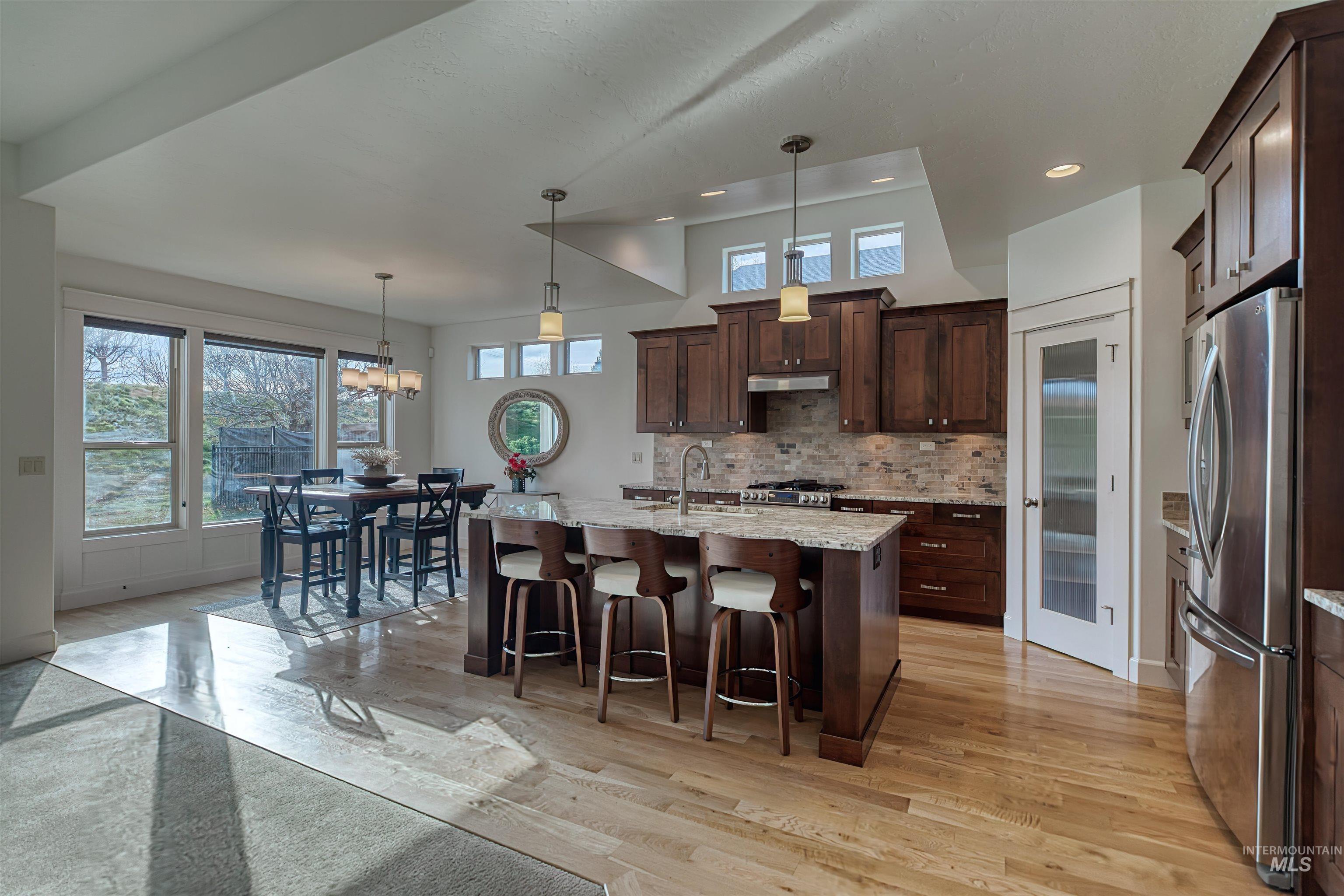 Kitchen with hanging light fixtures, stainless steel appliances, light stone counters, a kitchen bar, and a chandelier
