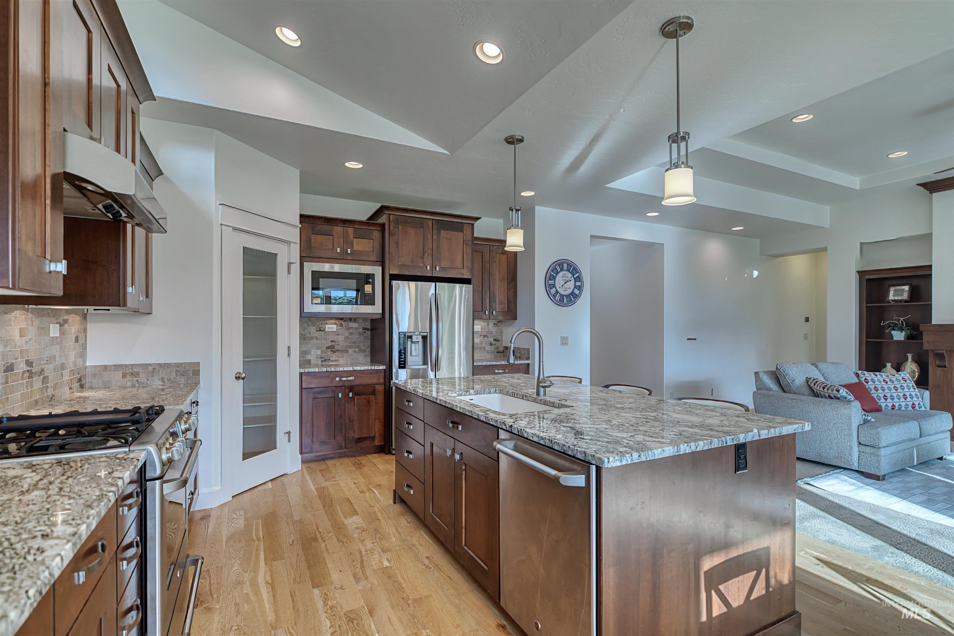 Kitchen with stainless steel appliances, decorative light fixtures, light stone counters, light wood-style flooring, and open floor plan