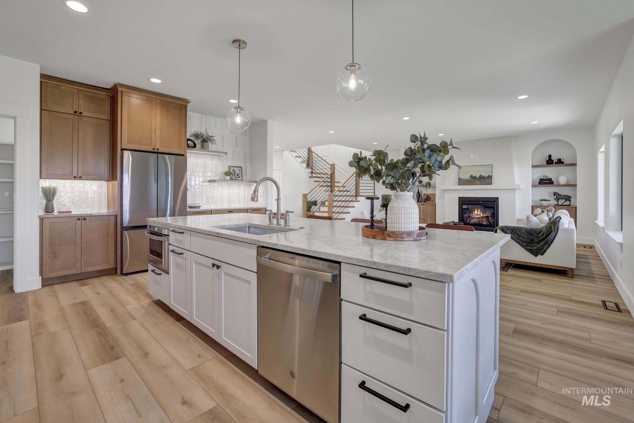 Kitchen with white cabinets, stainless steel appliances, decorative light fixtures, open floor plan, and a glass covered fireplace