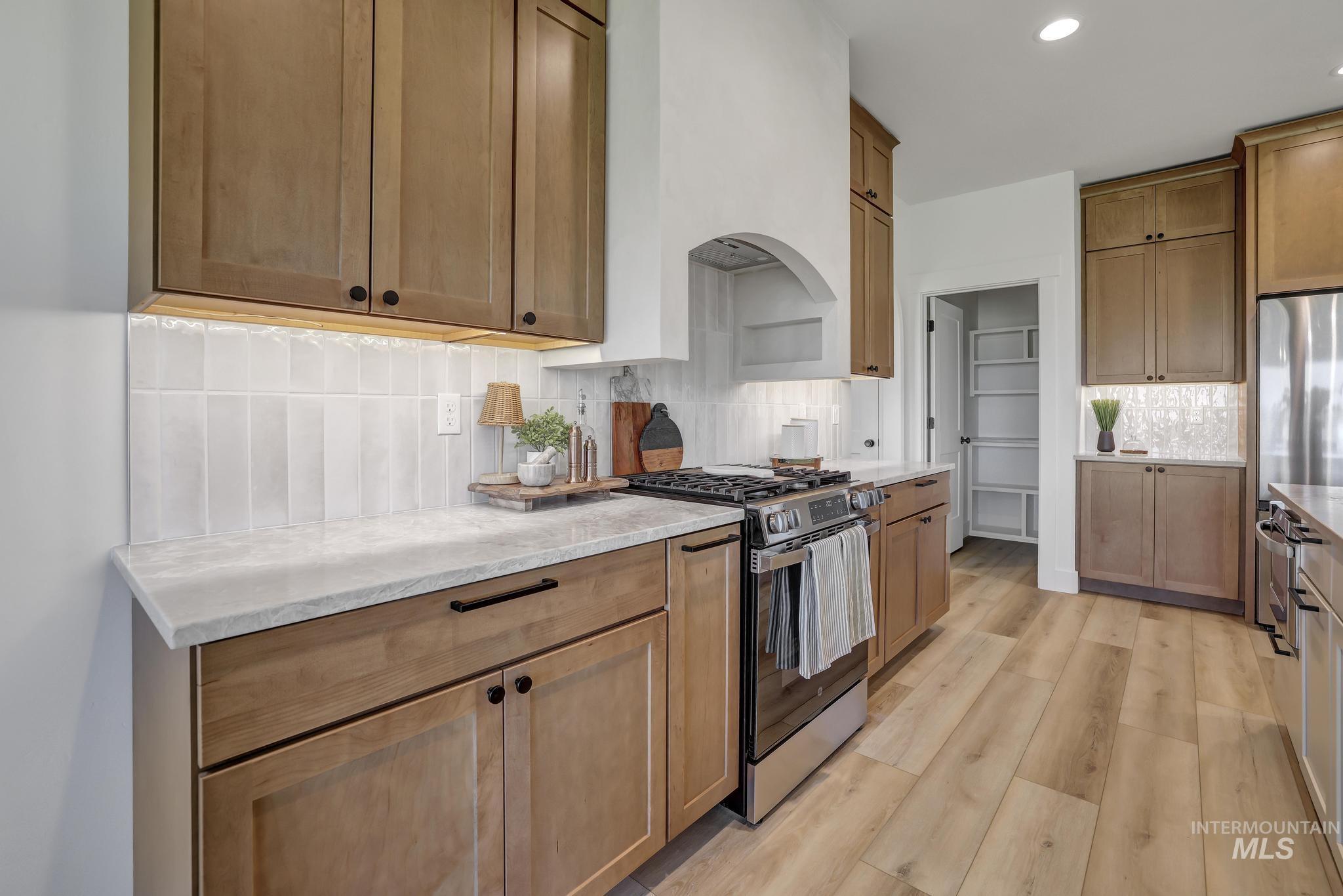 Kitchen with stainless steel appliances, decorative backsplash, brown cabinets, light stone counters, and recessed lighting