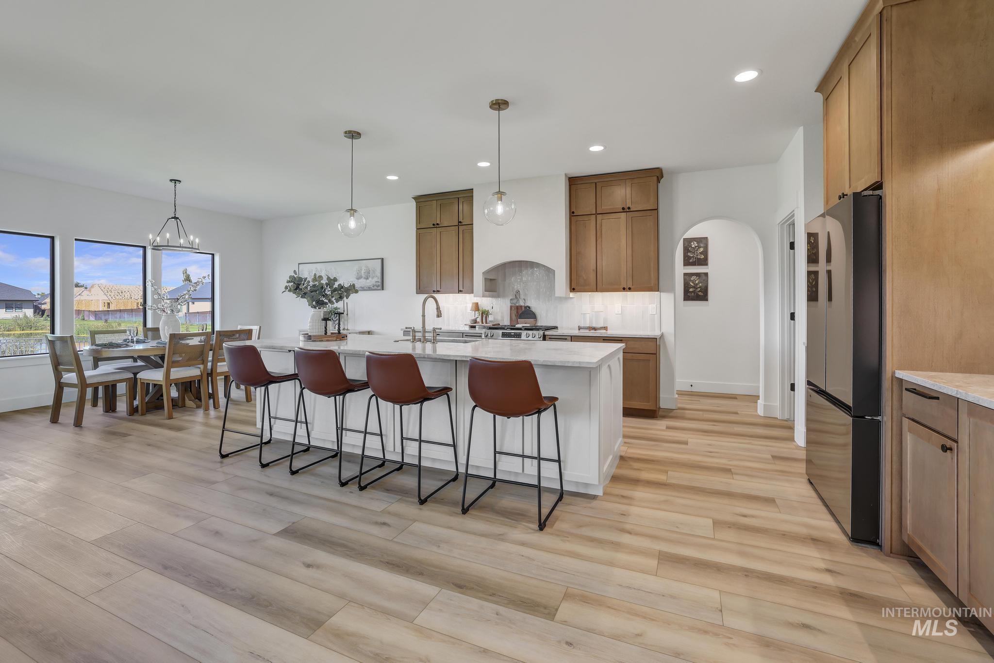 Kitchen featuring hanging light fixtures, brown cabinets, a kitchen breakfast bar, freestanding refrigerator, and a center island with sink