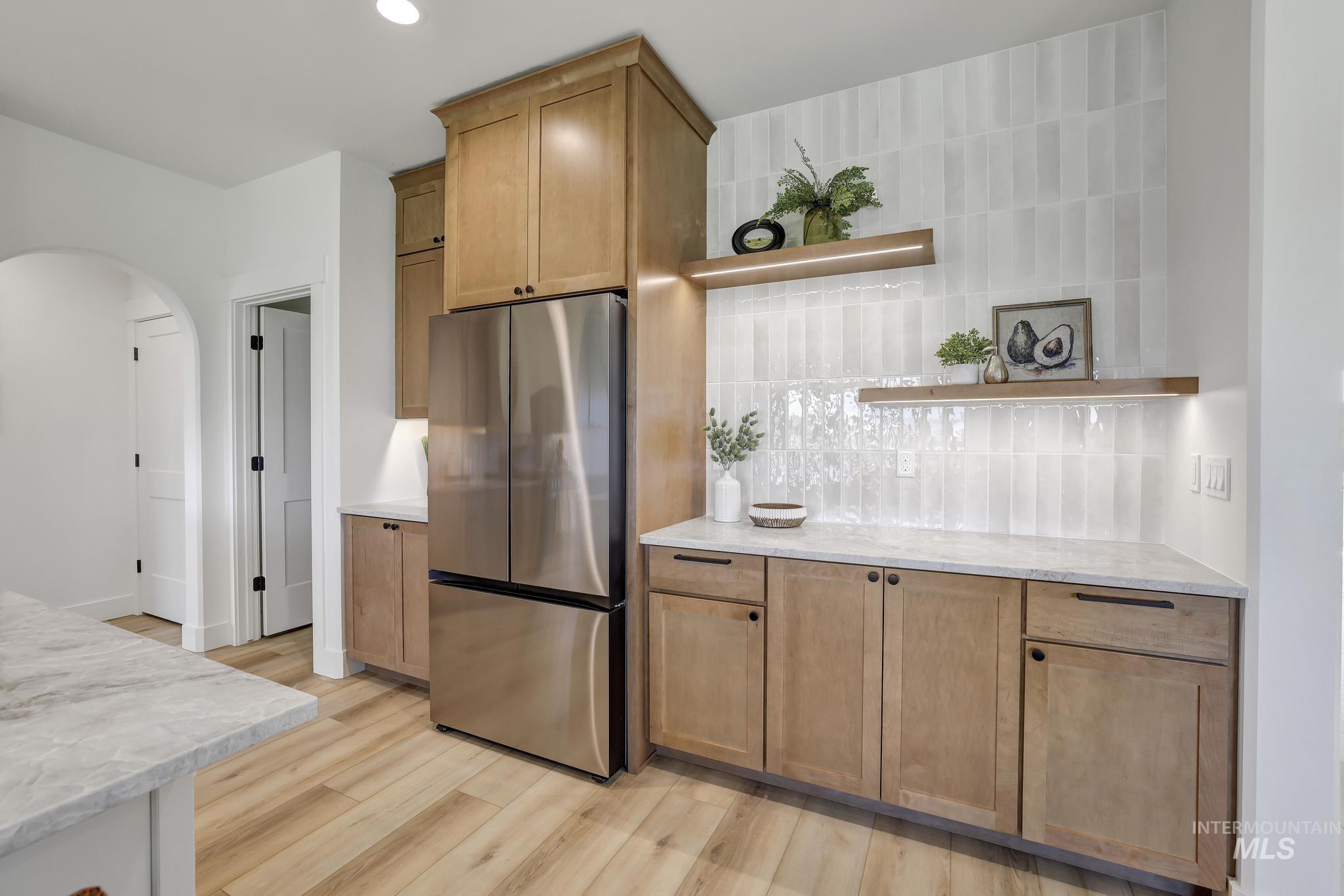 Kitchen featuring open shelves, freestanding refrigerator, arched walkways, tasteful backsplash, and light wood-style flooring