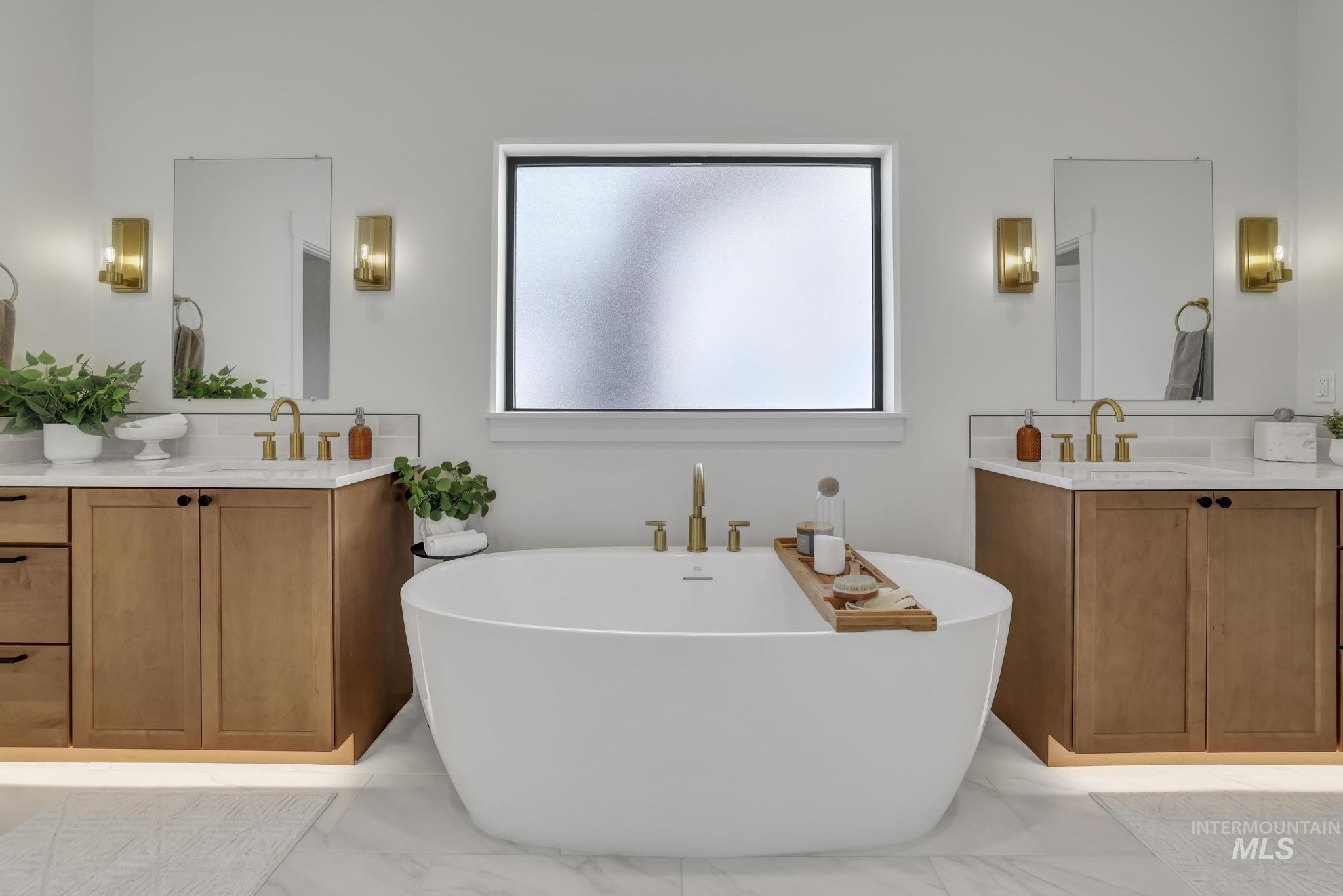 Bathroom with two vanities, a soaking tub, and light marble finish flooring