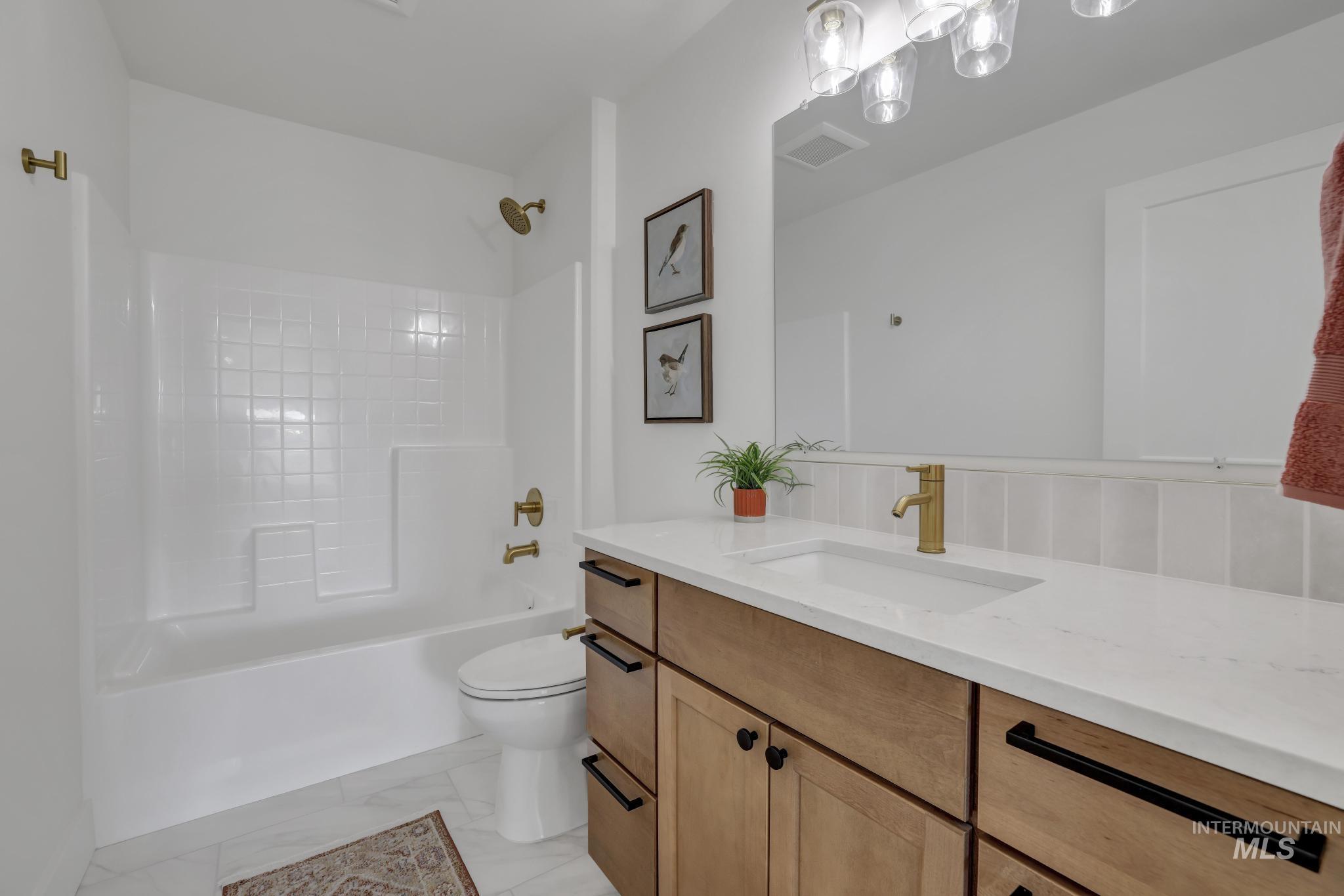 Bathroom featuring washtub / shower combination, vanity, and light marble finish flooring
